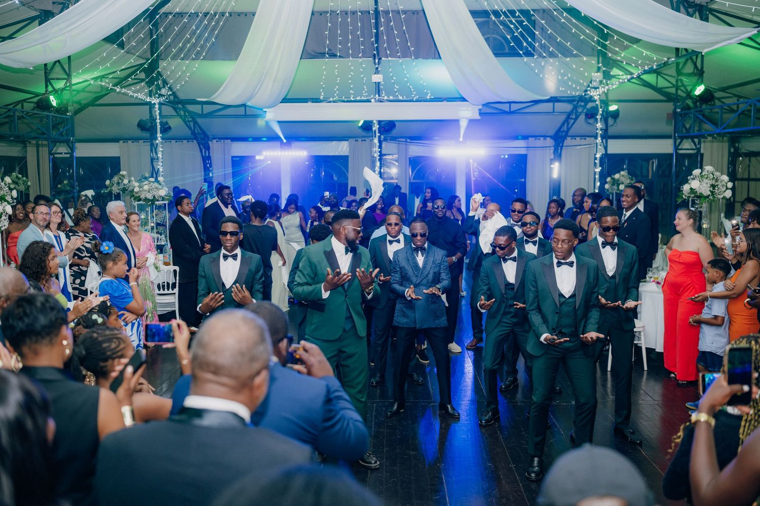 Wedding reception venue with blue and green lighting effects and elegant white draping.