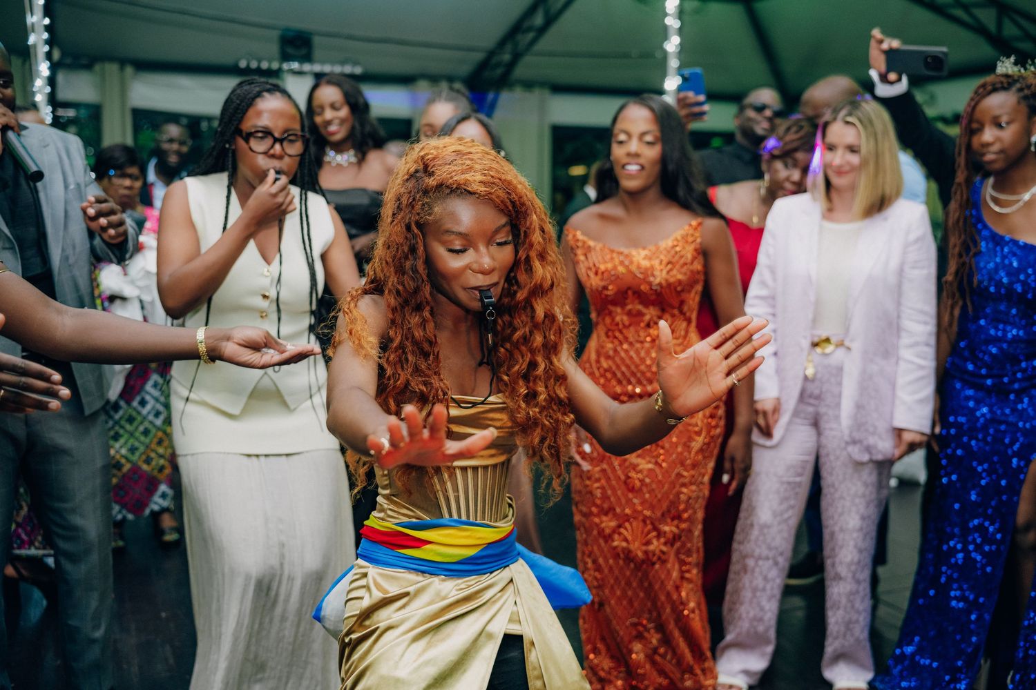 Festive reception scene with guests in colorful formal attire dancing and socializing.