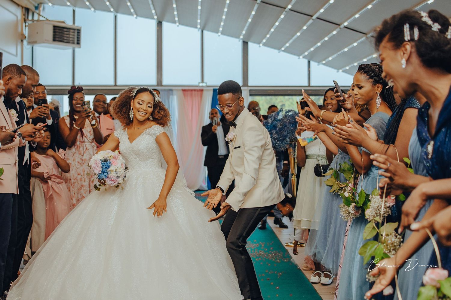 Joyful celebration with wedding party dancing down teal carpet aisle during reception.