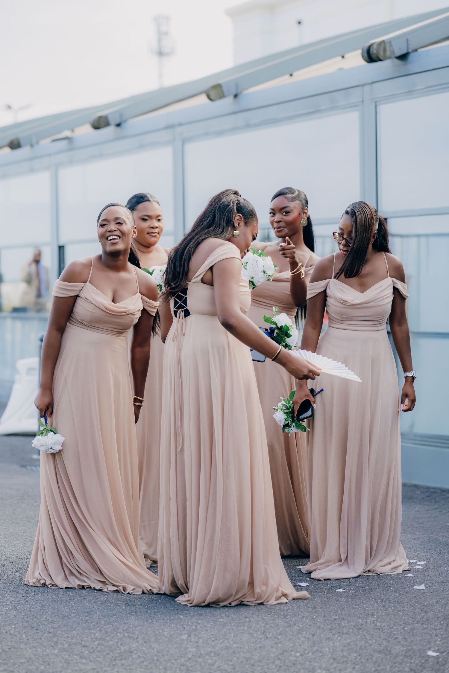 Bridesmaids in flowing blush pink off-shoulder dresses laugh together during wedding party photos.