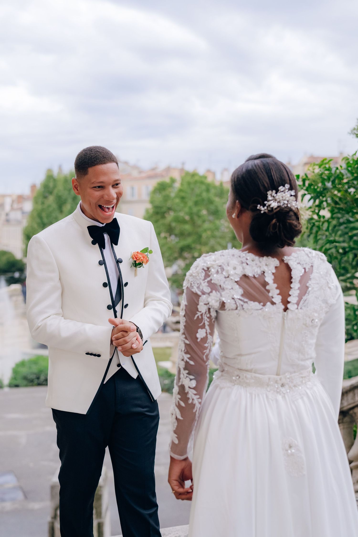 A romantic wedding couple shares a joyful moment together in a garden setting wearing white and black formal attire.