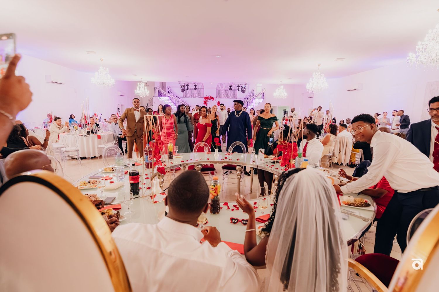 Wedding reception guests dancing and celebrating on a dance floor under pink lighting at an indoor venue.