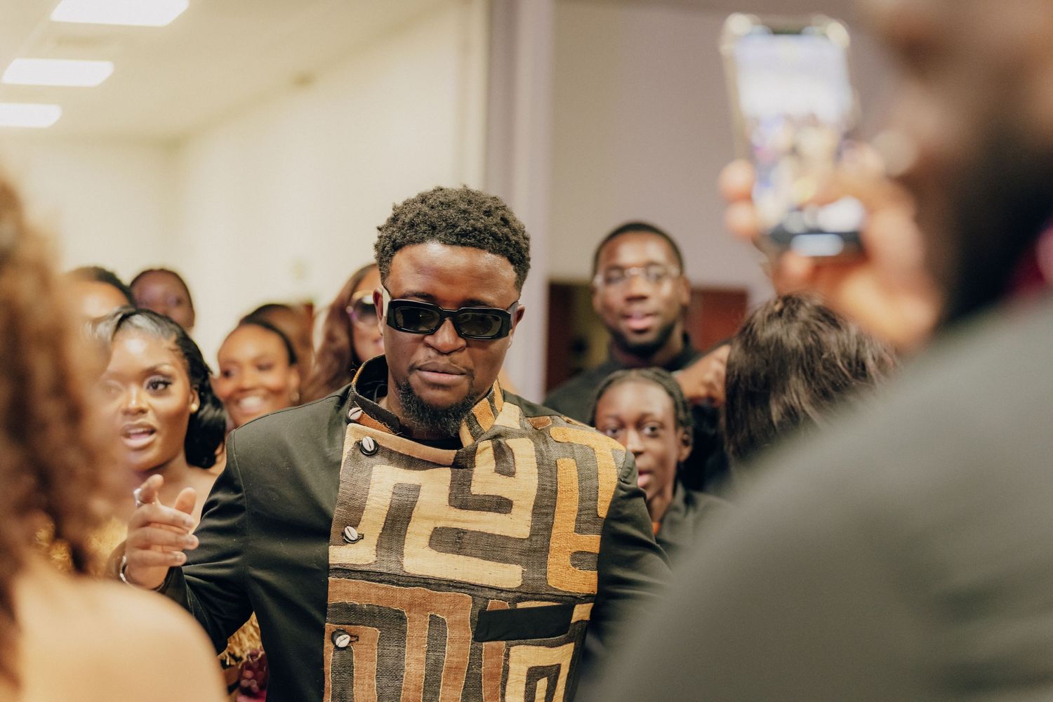 A stylish guest wearing sunglasses and geometric pattern outfit mingles at an event.