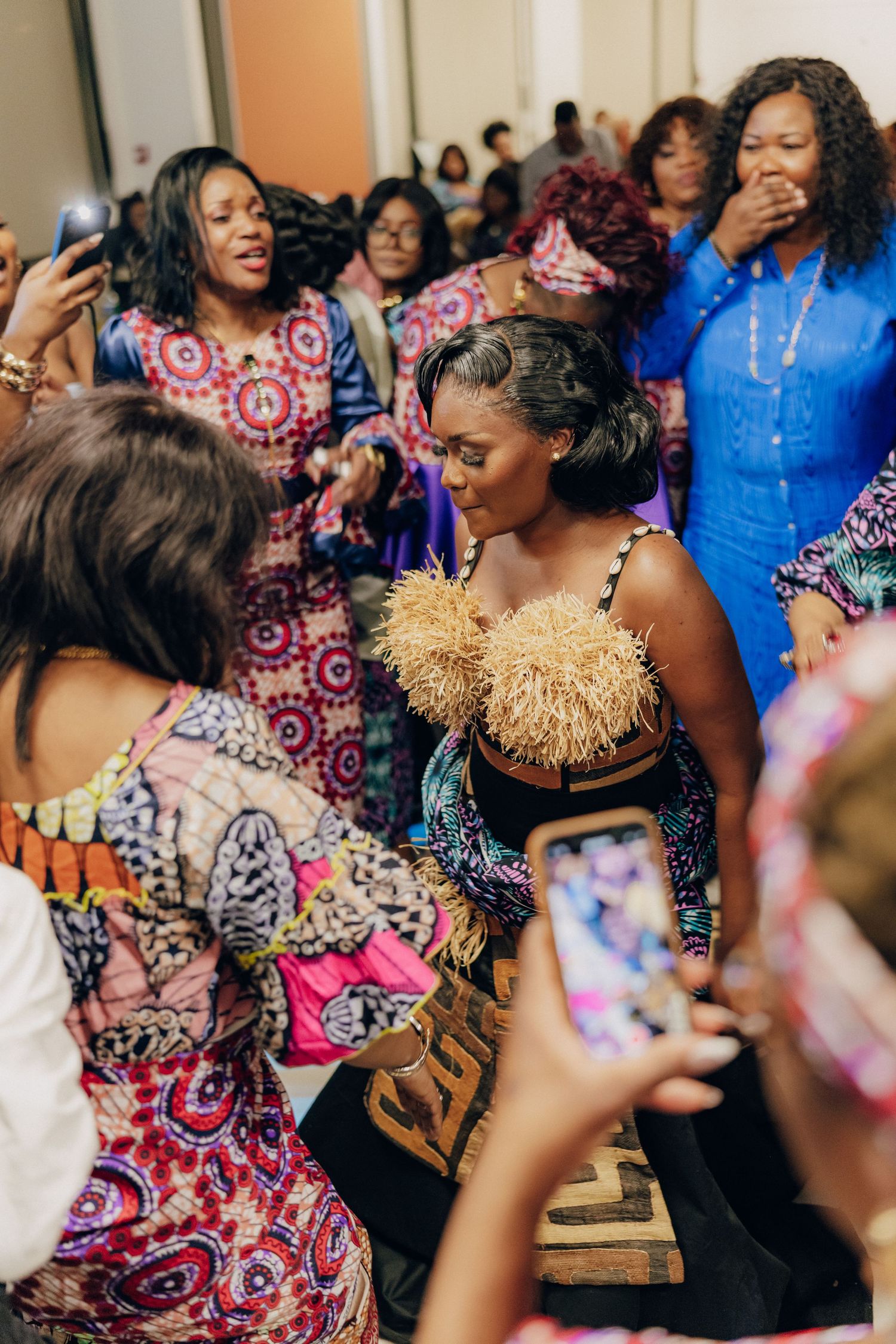 A joyful celebration with attendees in colorful African prints and traditional dress gathered around taking photos.