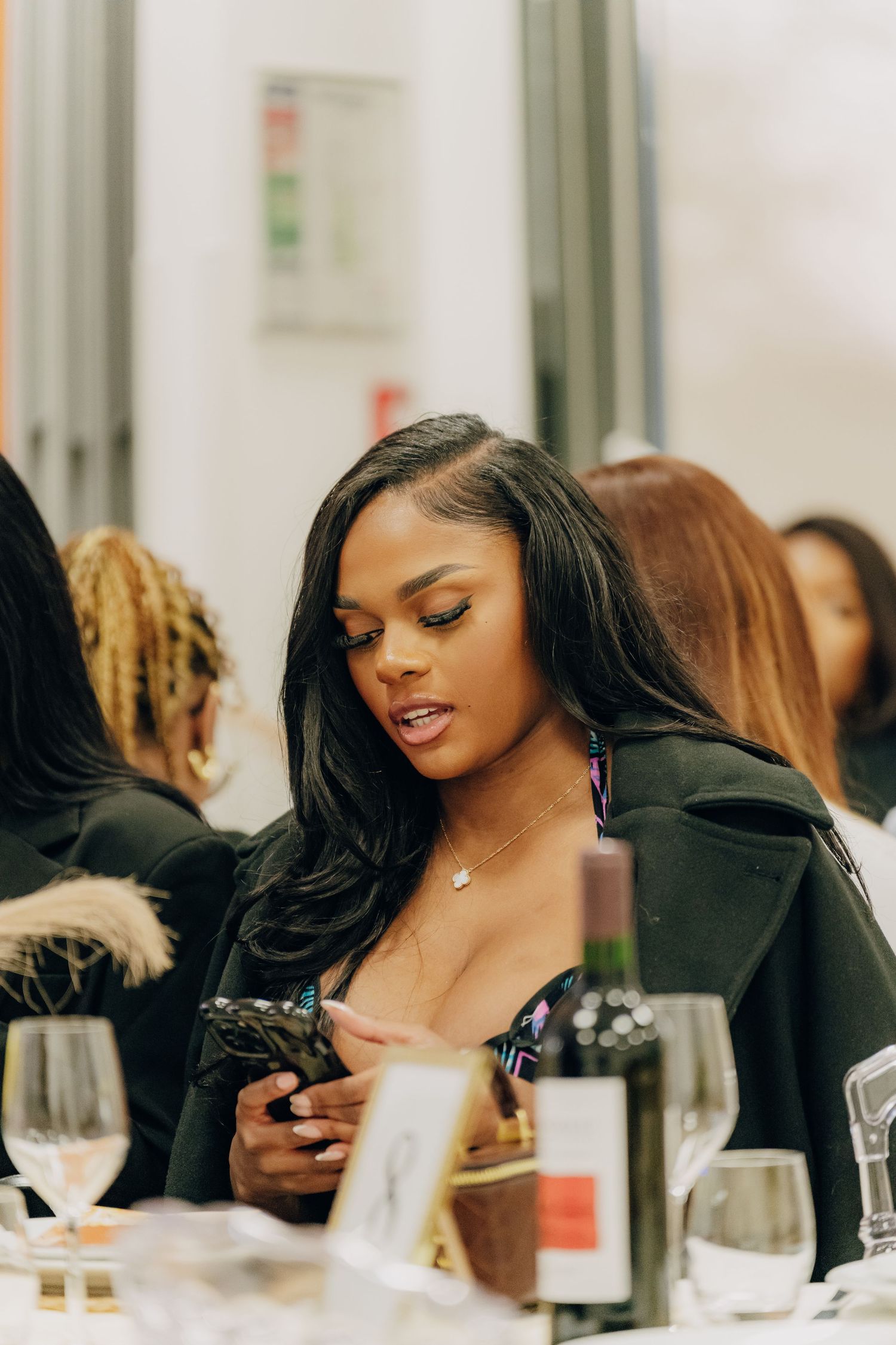 Person at dining table checking their phone during social gathering with wine glasses and table settings.