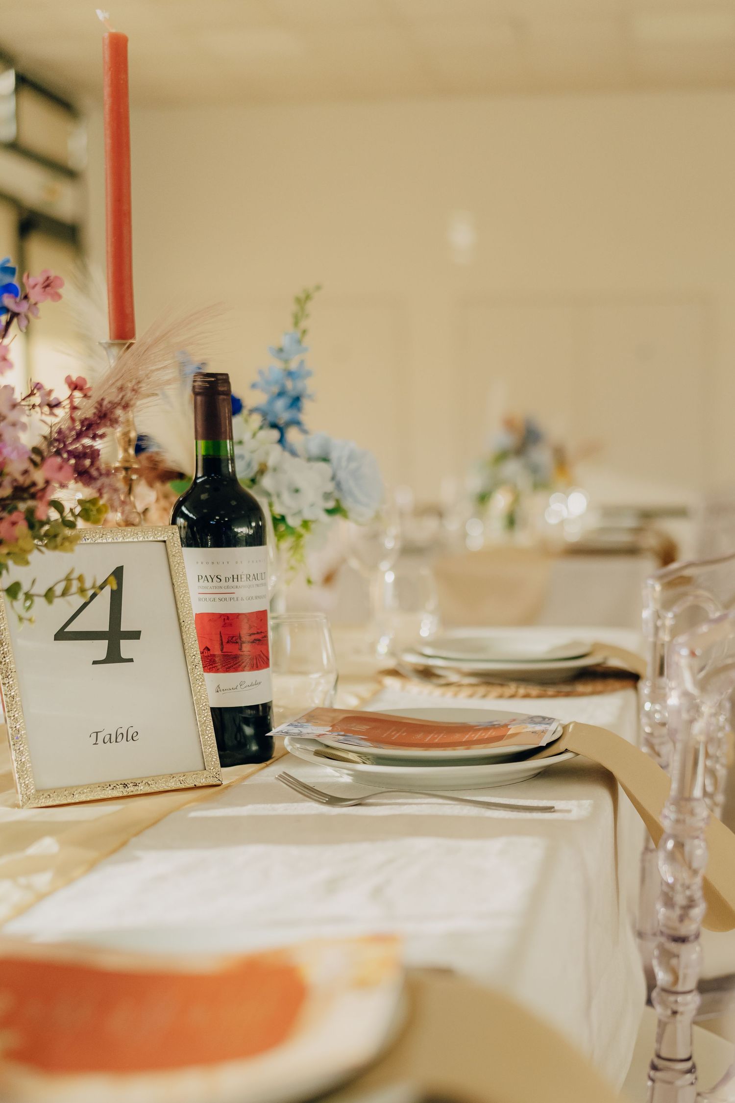 Elegant table setting with a table number 4, wine bottle, and delicate floral centerpiece in pink and blue blooms.