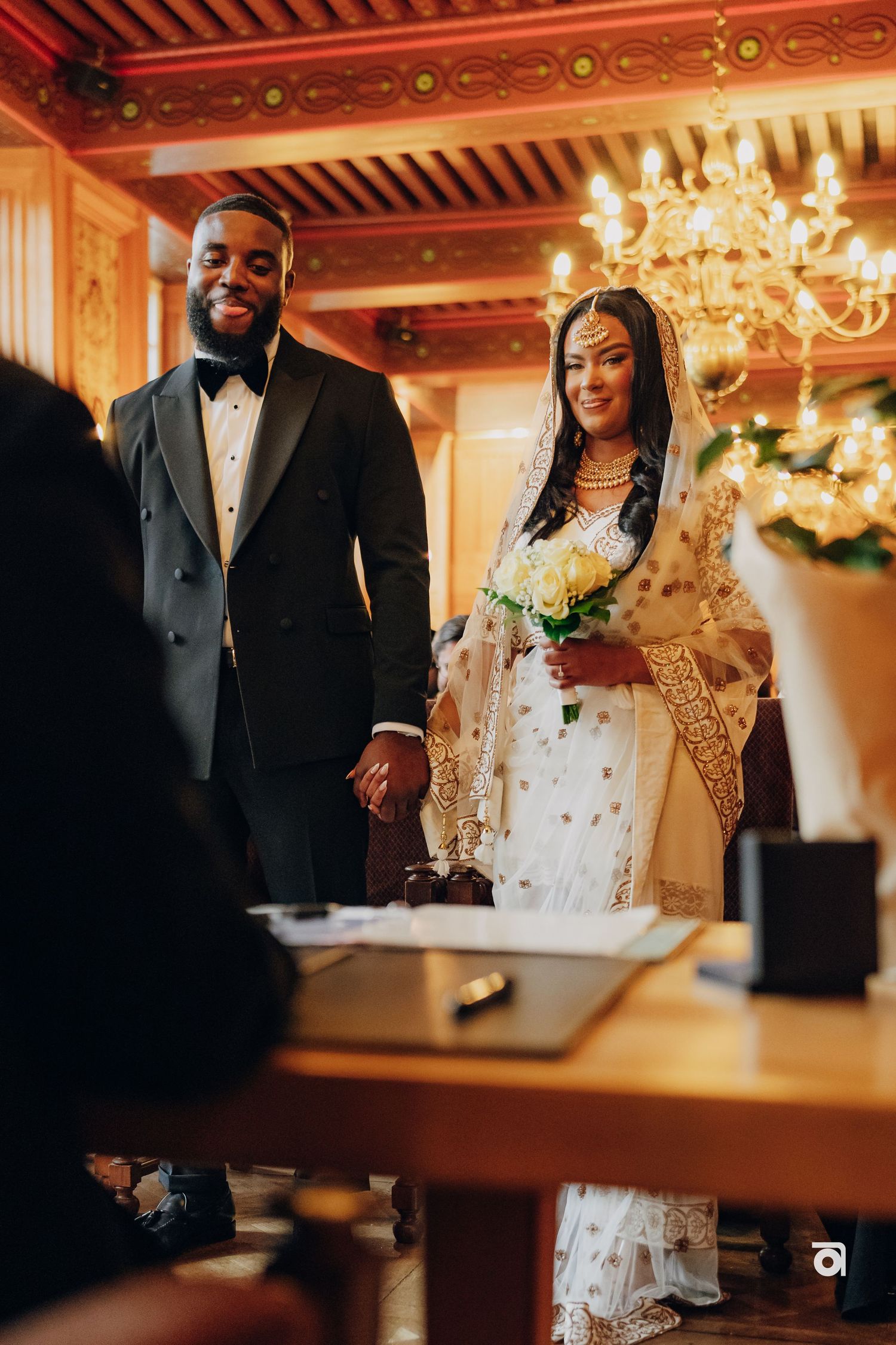 A wedding ceremony in an ornate room with a chandelier as a couple stands at a table during the signing.
