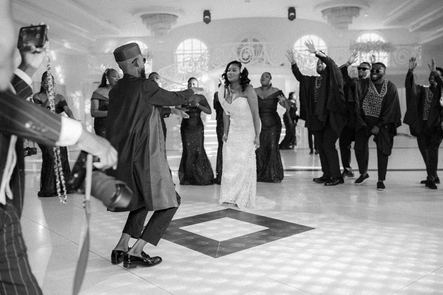Black and white photo of wedding guests dancing energetically on a checkered dance floor.