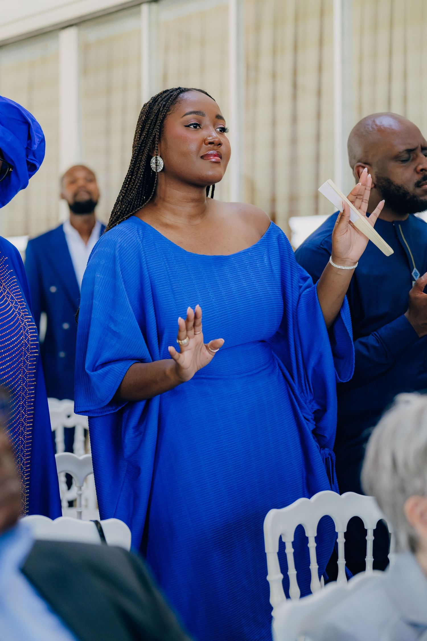 A woman in a flowing royal blue dress raises her hands during what appears to be a wedding celebration.