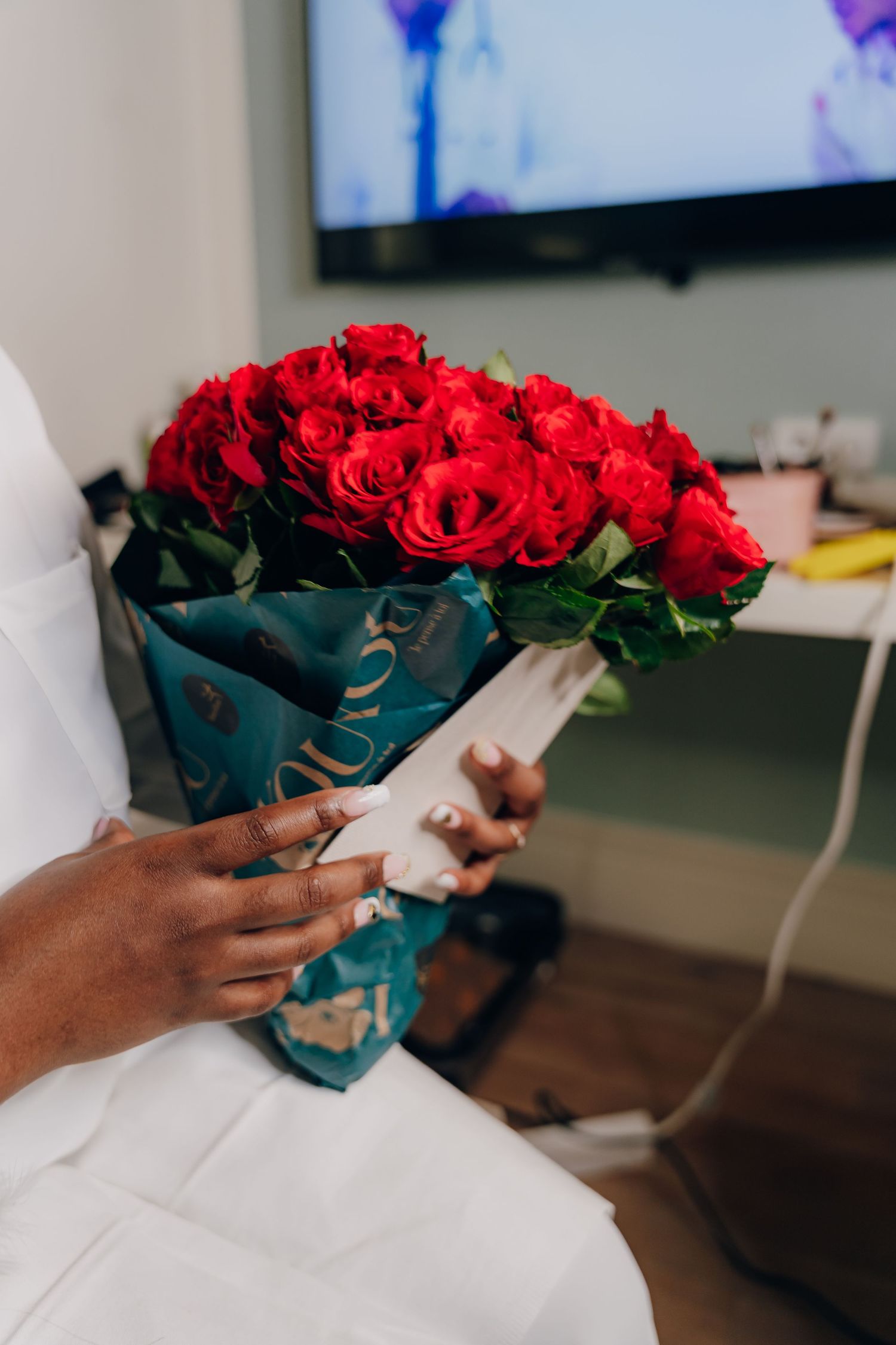 Hands holding a beautiful arrangement of red roses in a teal-colored vessel.