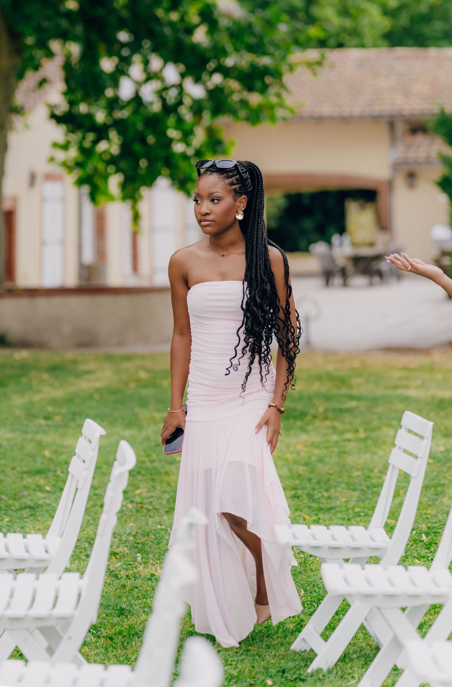 A person in a white strapless dress poses gracefully on a lawn with white chairs arranged in the background.