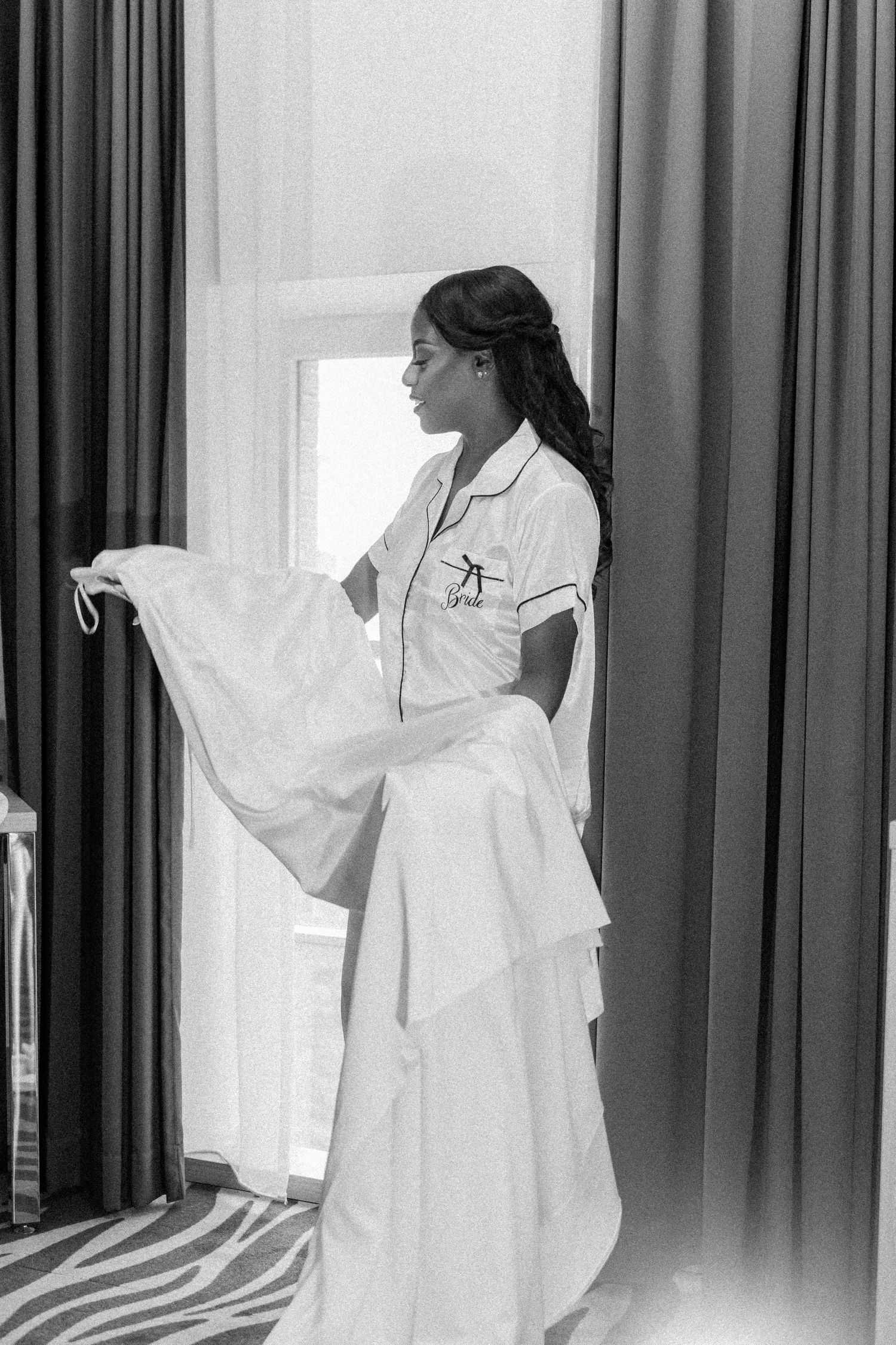 A person in a flowing white dress poses gracefully against a dark curtain background.