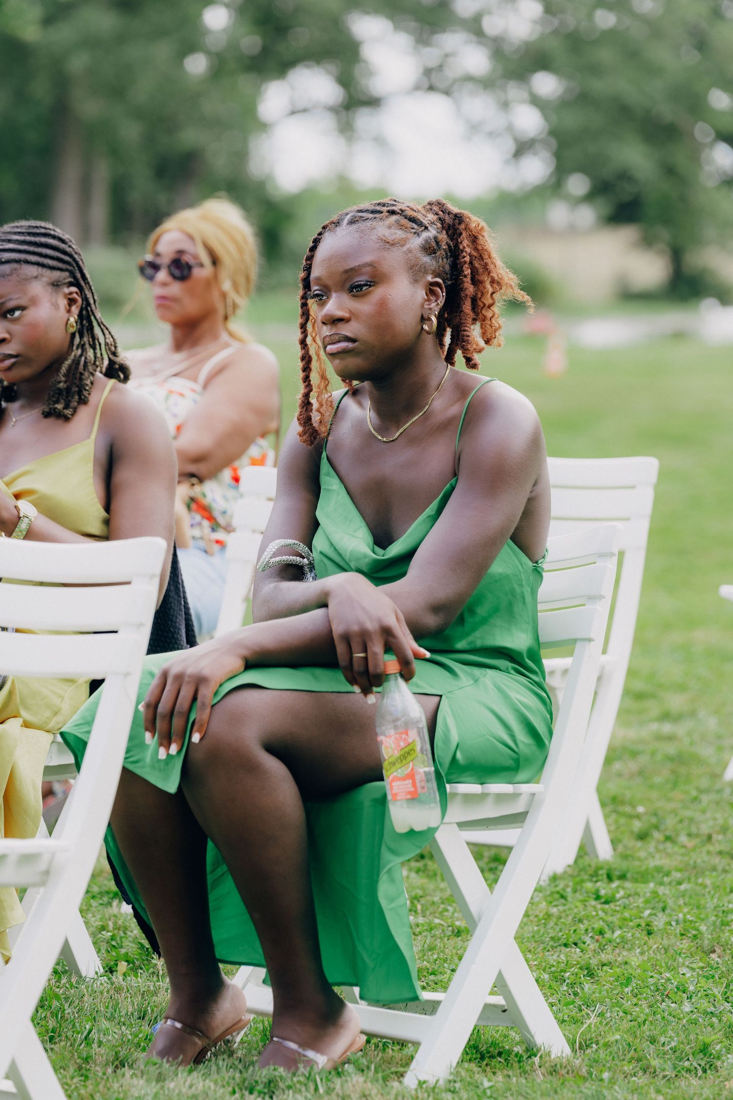 Guests in vibrant green dresses seated on white chairs during an outdoor event.