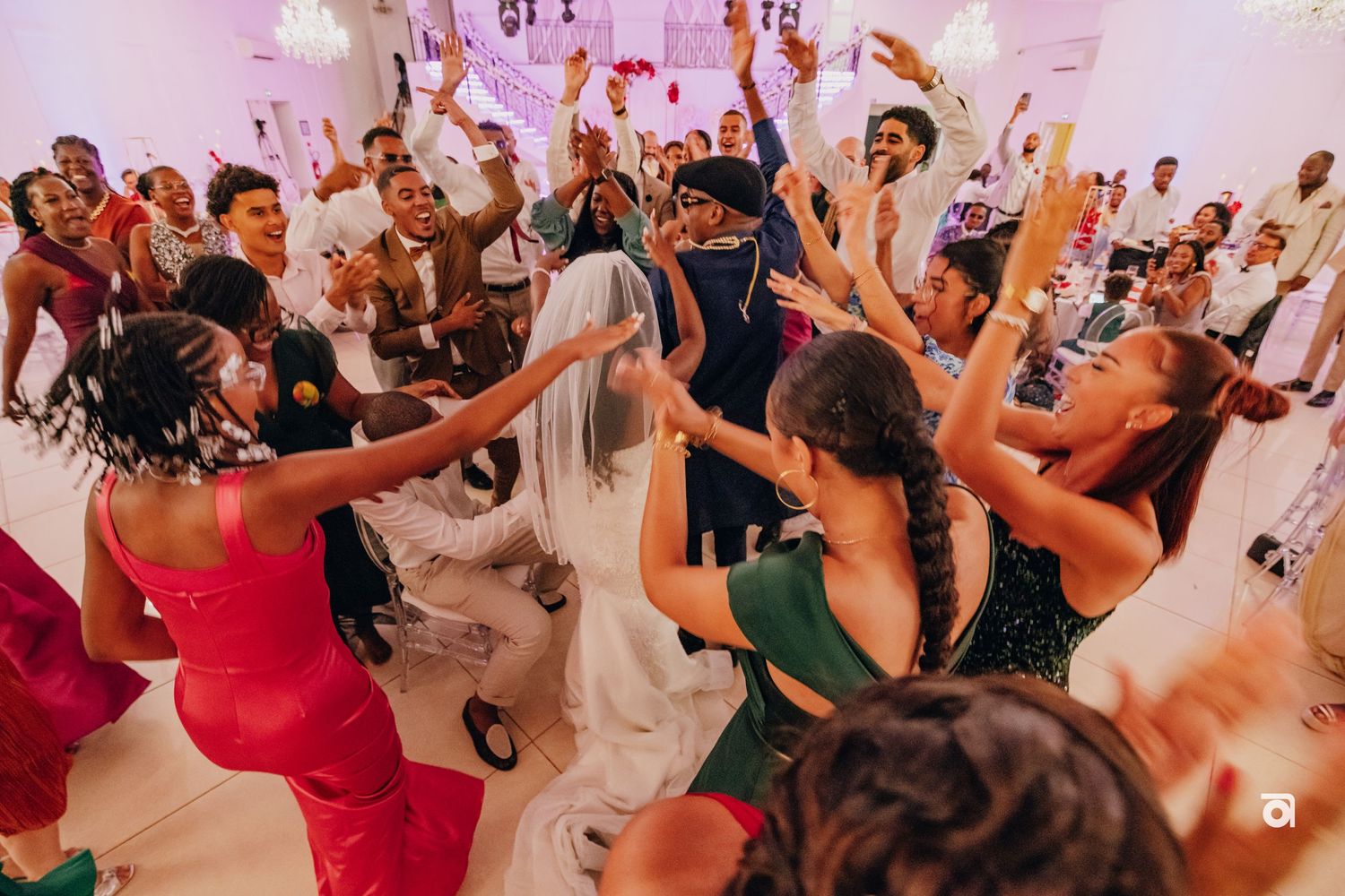 Energetic crowd dancing and celebrating at an upscale wedding reception in a white decorated venue.