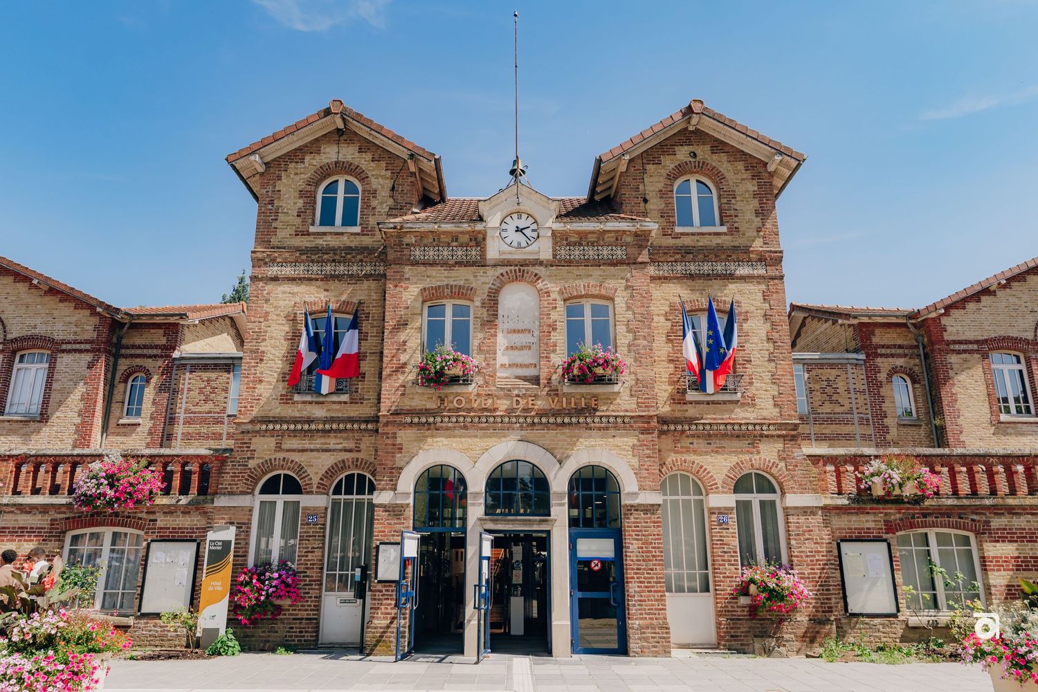 Historic French municipal building with twin gables and French flags displaying ornate stone architecture.