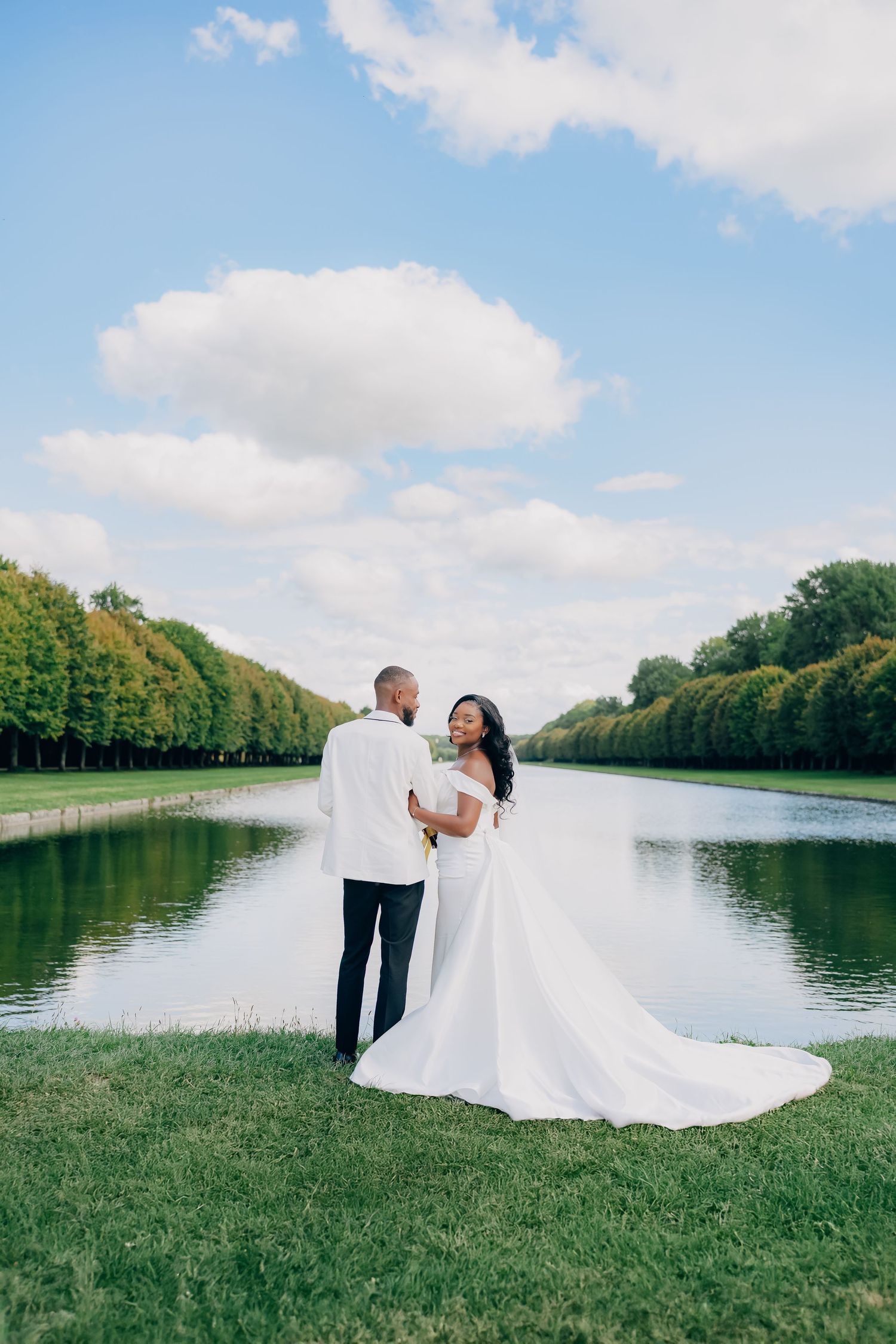 A couple in wedding attire shares romantic moments by a serene lake surrounded by trees on their special day.
