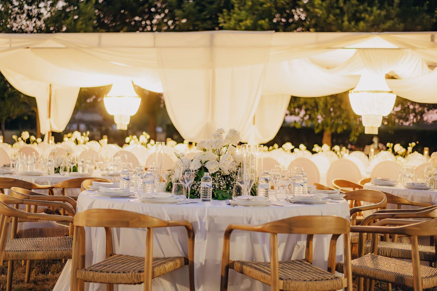 White wedding tent reception setup with elegant tables, chairs, and hanging lanterns creating a romantic atmosphere.