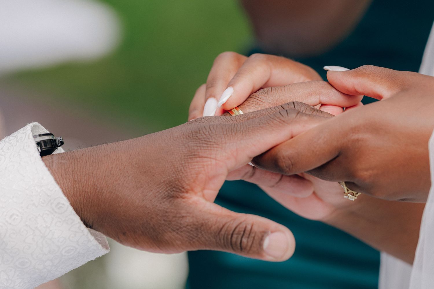 Close-up of hands exchanging rings during an outdoor wedding ceremony.