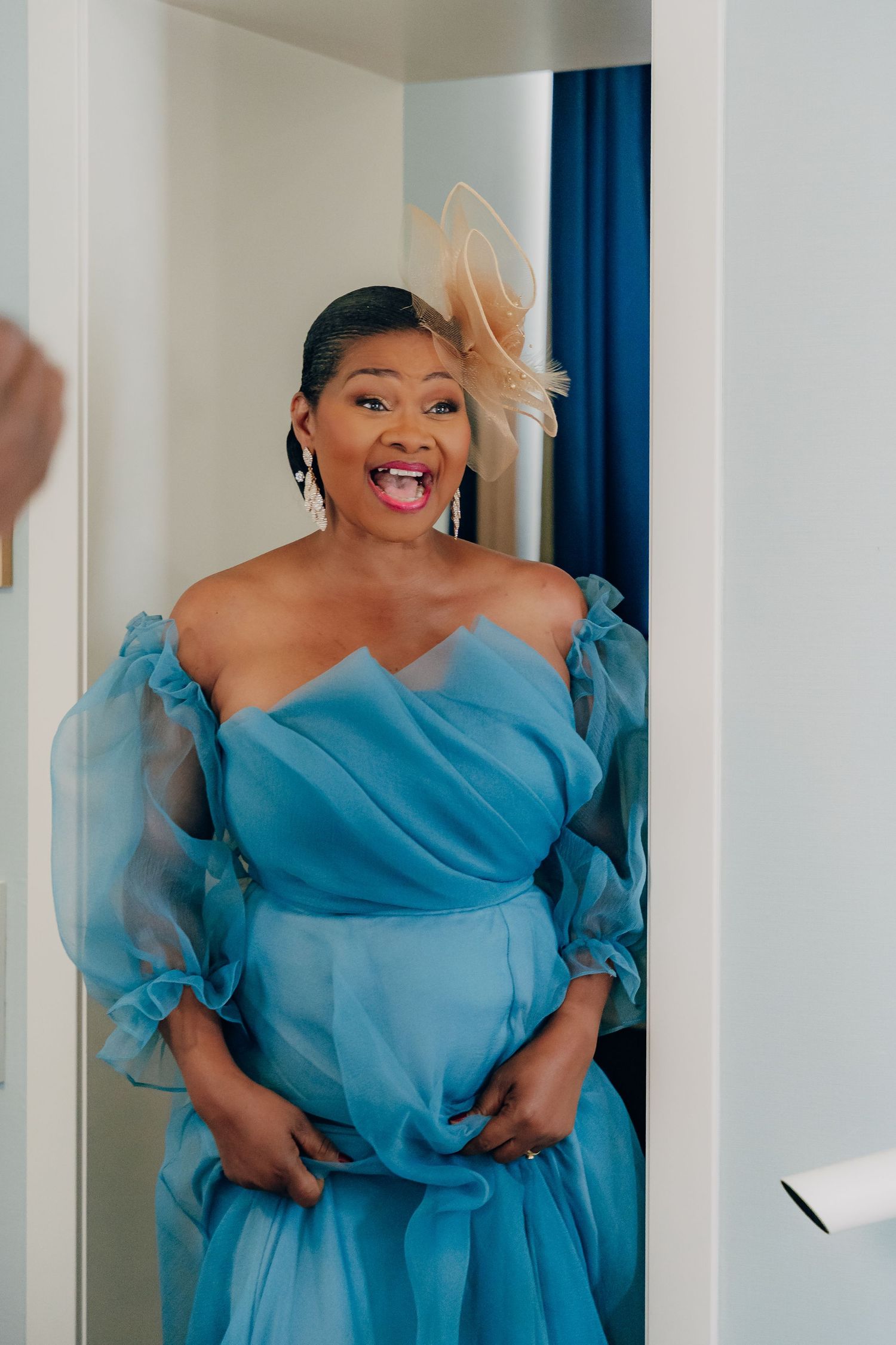 A person in a flowing blue gown shows joy and excitement in a bright white space.