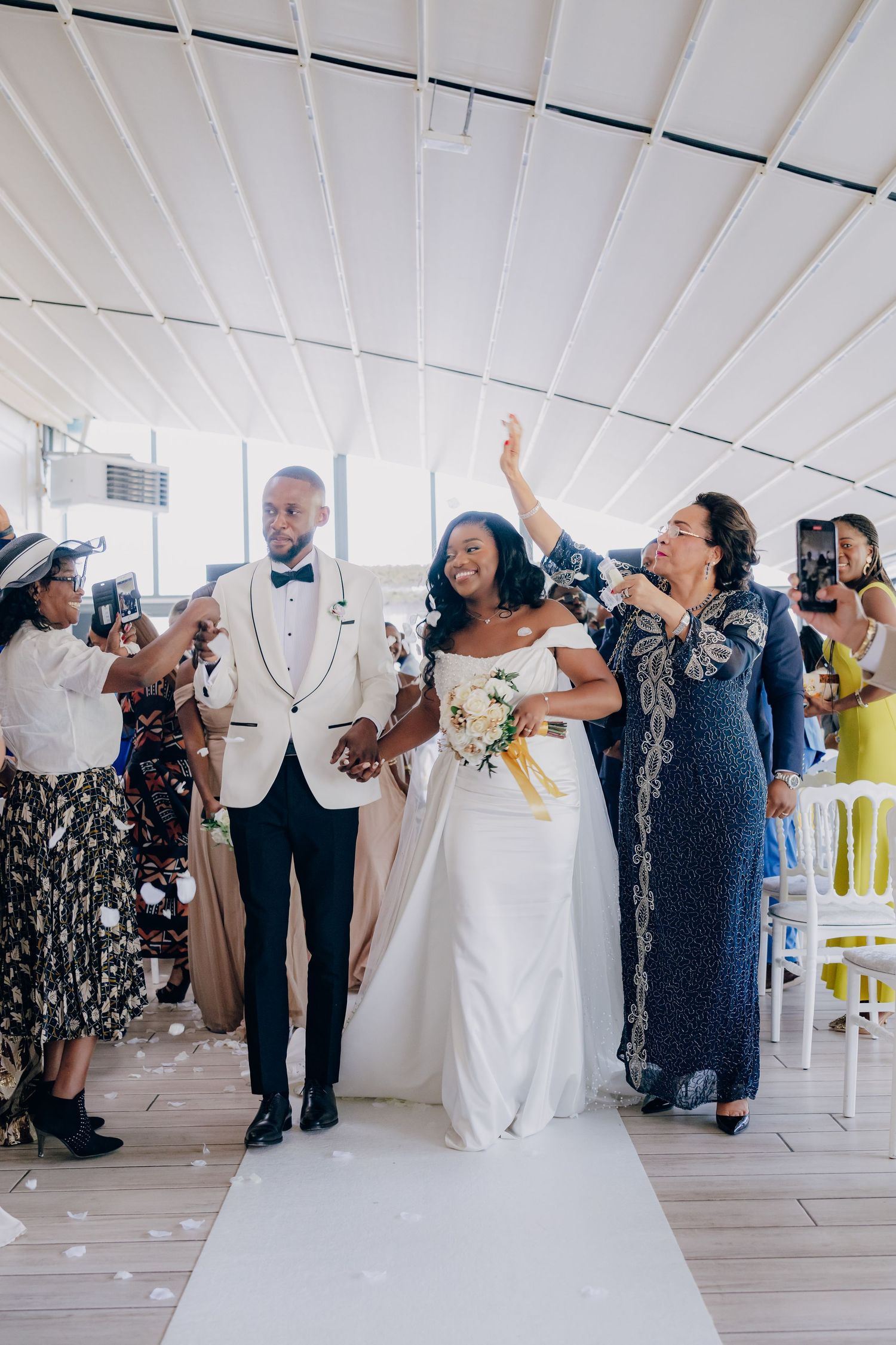 Wedding celebration with guests cheering as the newlyweds walk down the aisle under confetti.