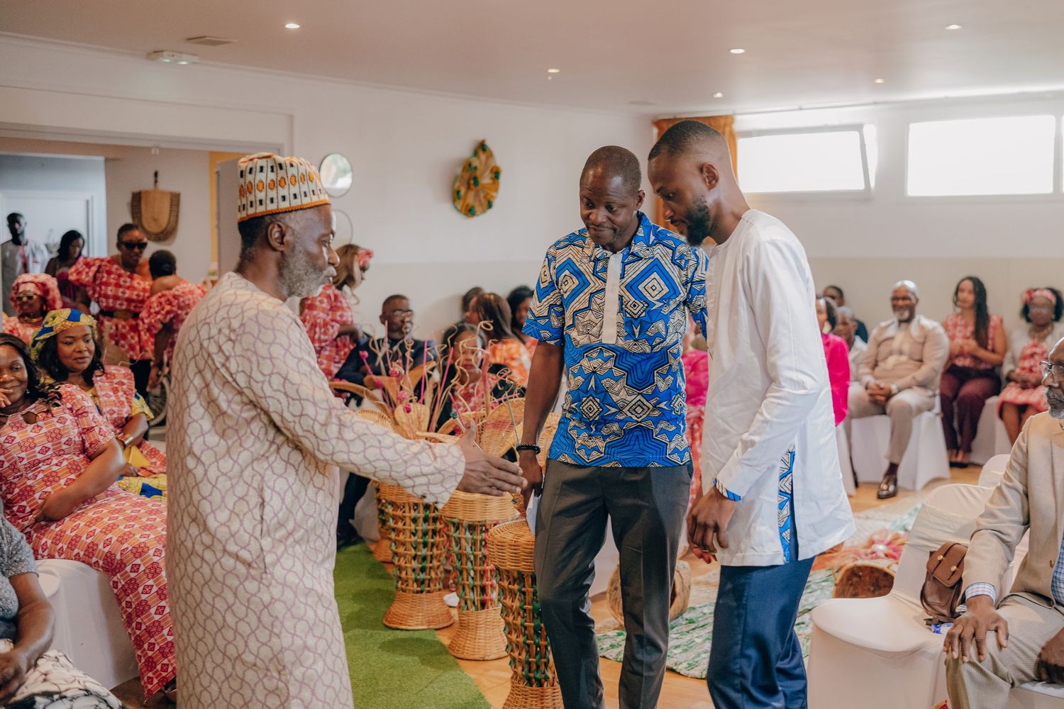 Wedding celebration showing guests in traditional African attire mingling and dancing in a bright indoor space.