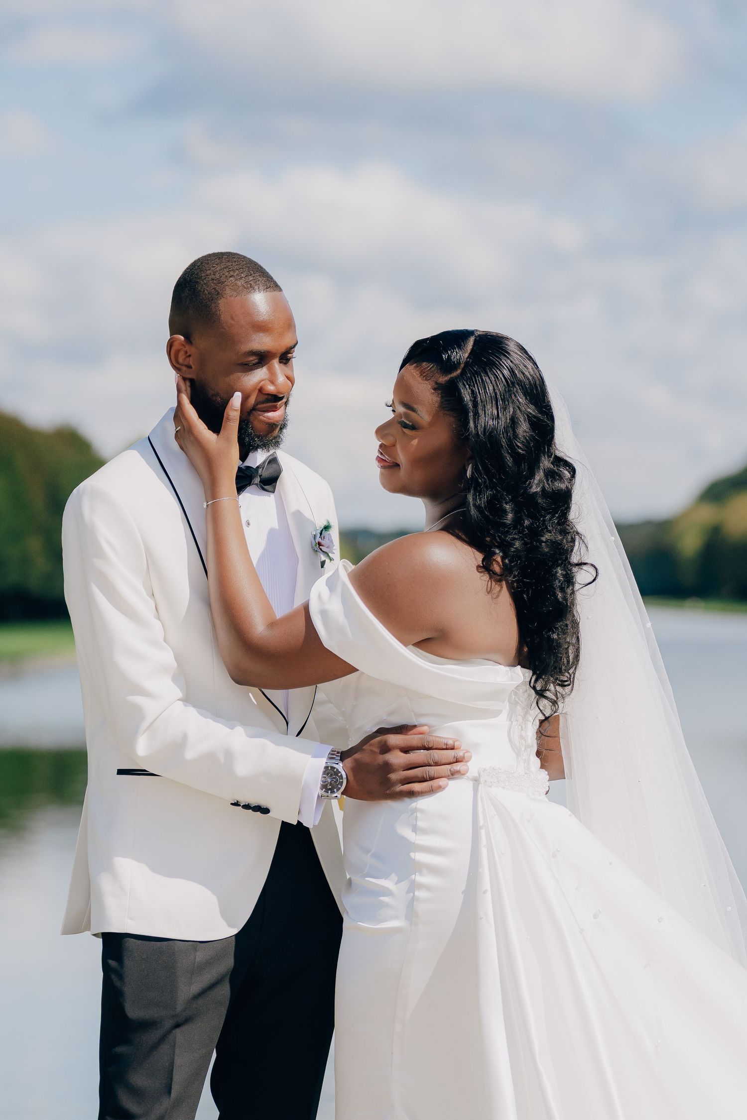 Romantic wedding couple shares intimate moments by a scenic waterfront in elegant white attire.