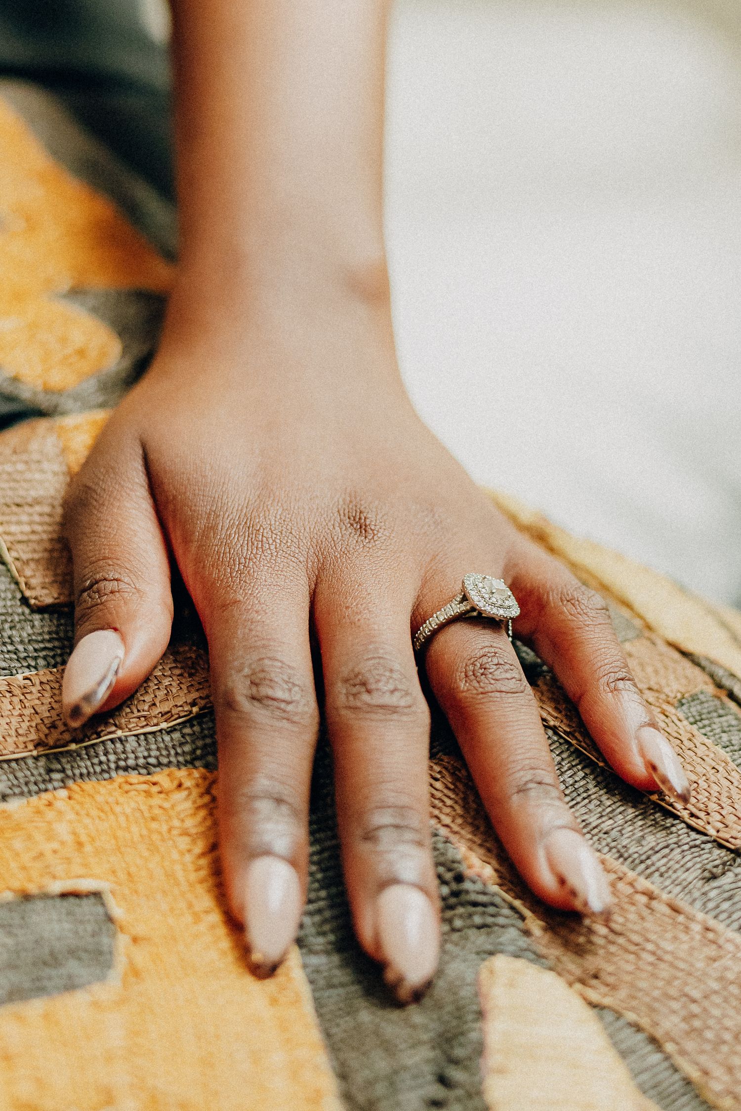 A hand wearing a sparkling diamond engagement ring rests on a textured orange and brown surface.