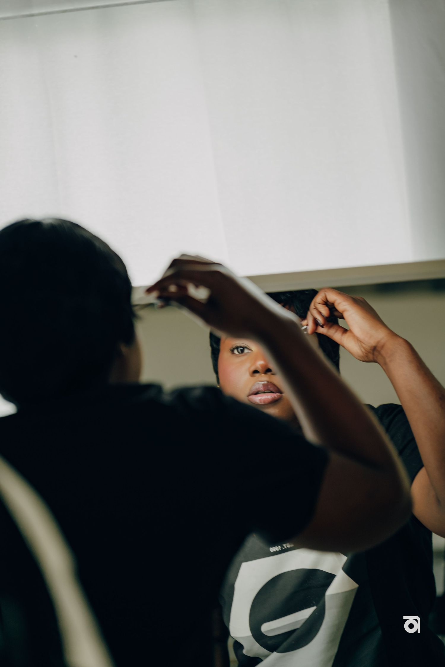 Person adjusting their detailed hairstyle while looking in a mirror with natural light streaming in.