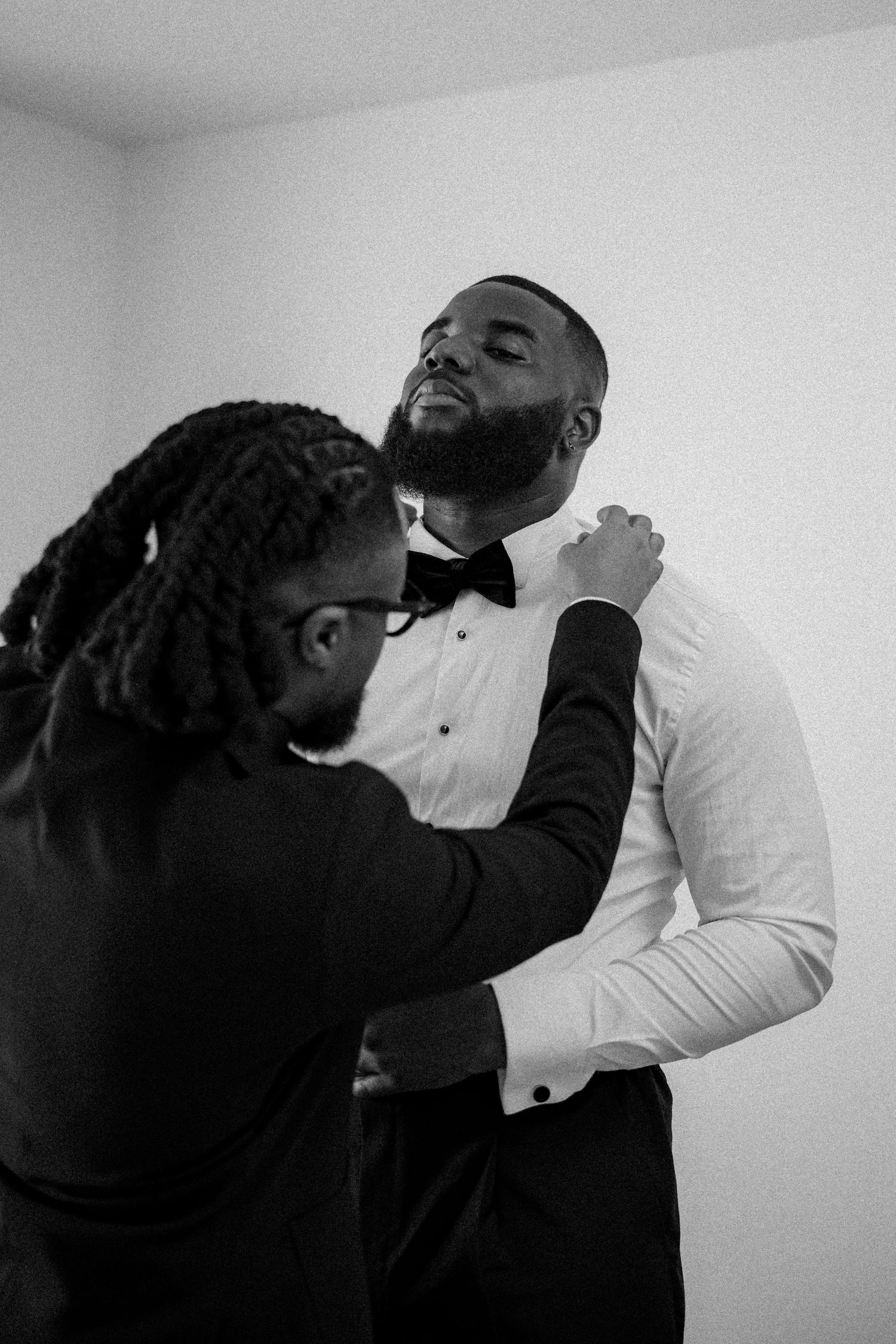 Black and white photo showing a person adjusting another's bowtie while getting ready in formal attire.