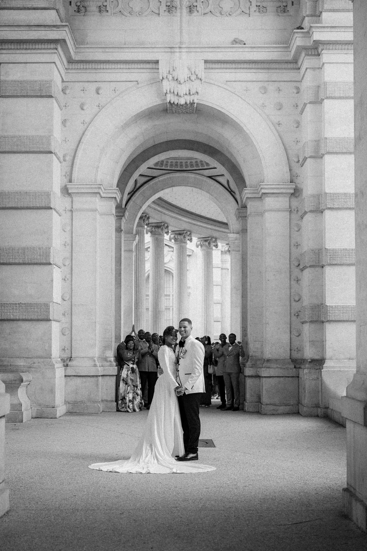 A couple shares an intimate moment under grand archways of a historic building in black and white photography.