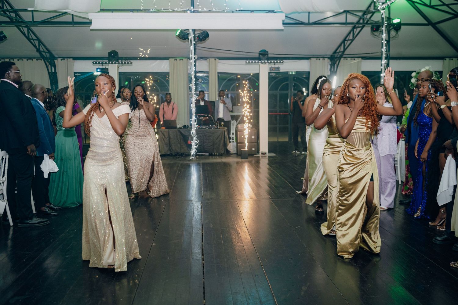 Wedding guests in formal attire dancing together during reception celebration.
