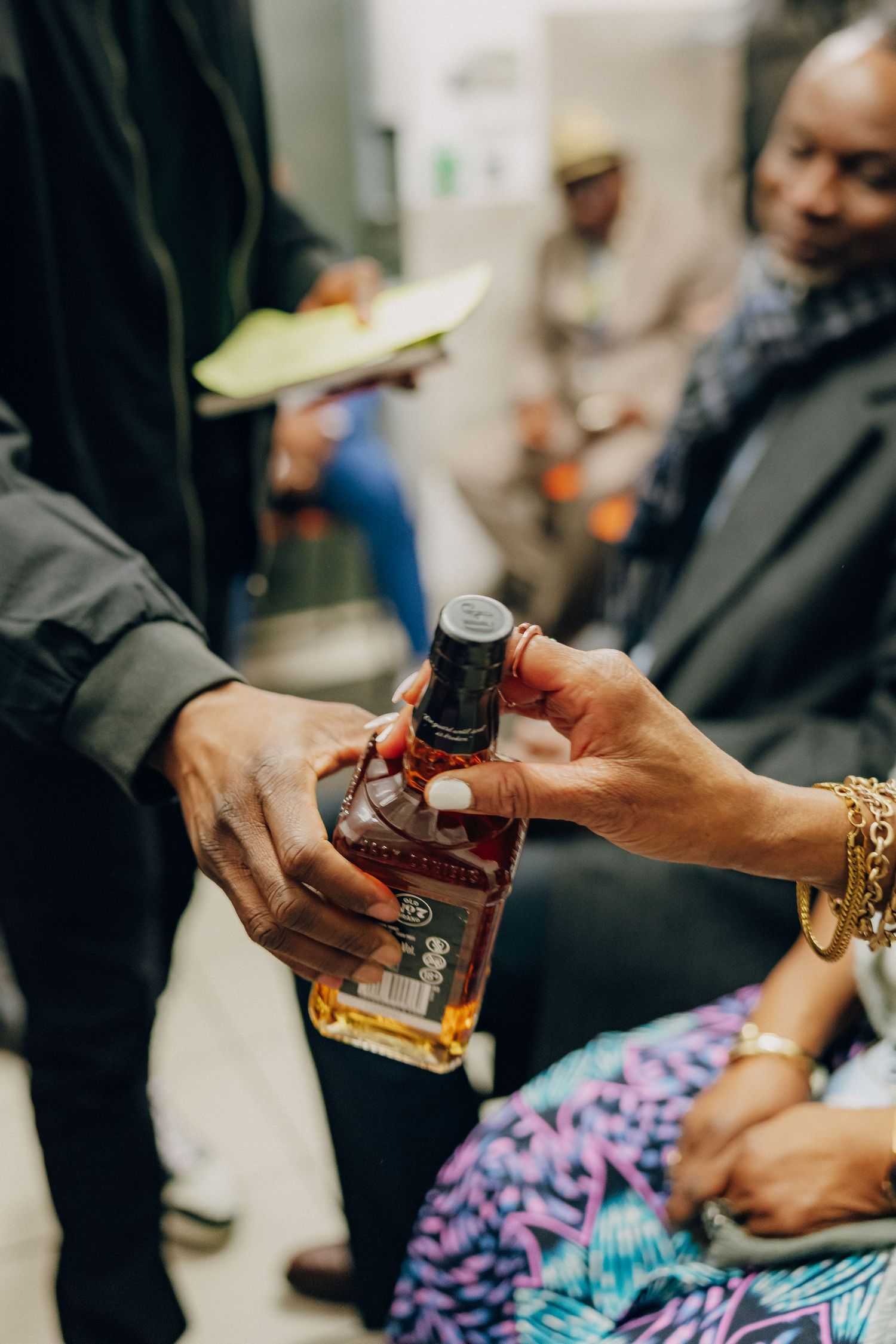 Two hands exchanging a bottle of brown liquor while holding a notepad.
