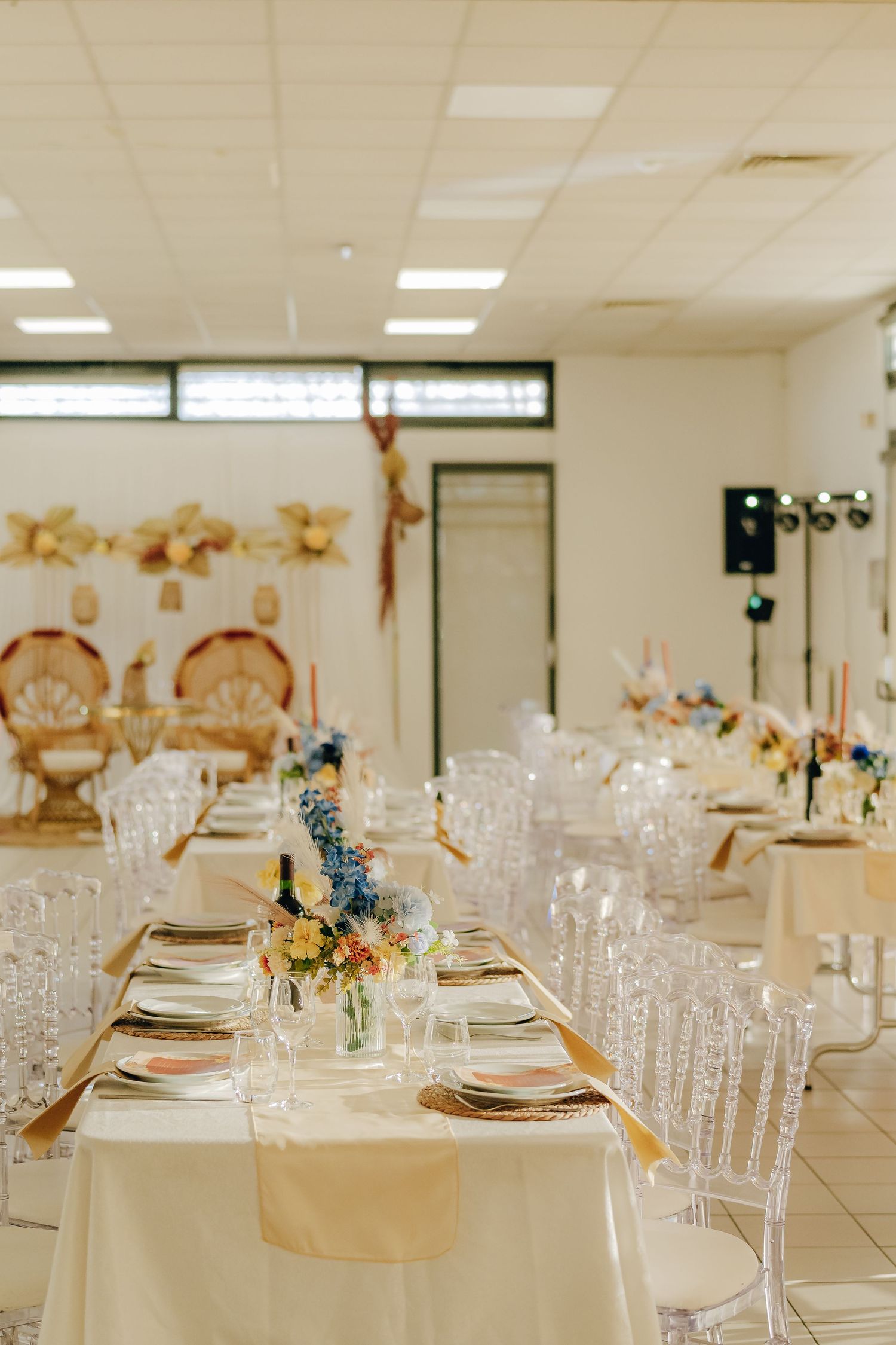 Elegant wedding reception table setup with clear chairs, white linens, and delicate floral centerpieces in an indoor venue.