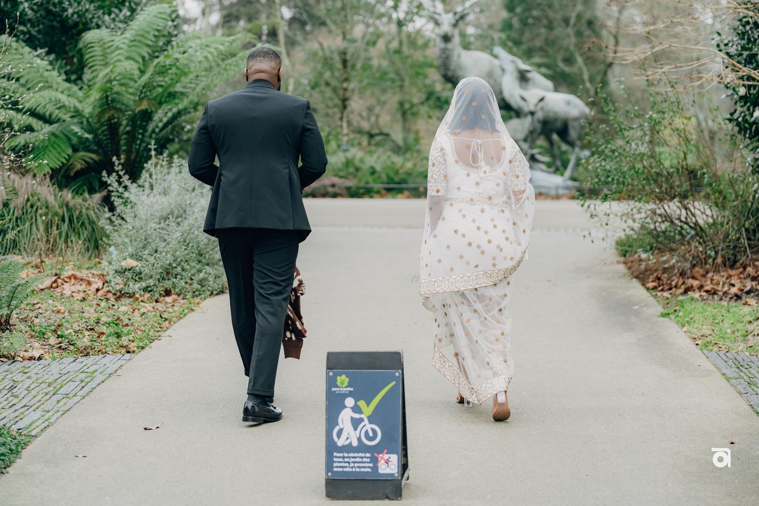 A couple walking down a garden path with someone pulling a bike share sign behind them.