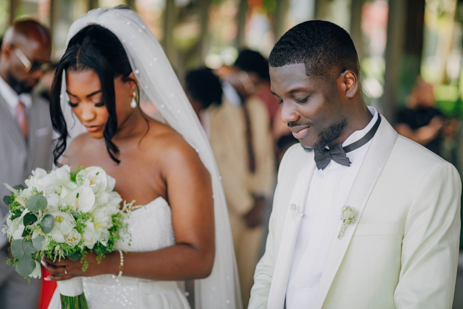 A couple shares an intimate moment during their wedding ceremony while holding a white bouquet.