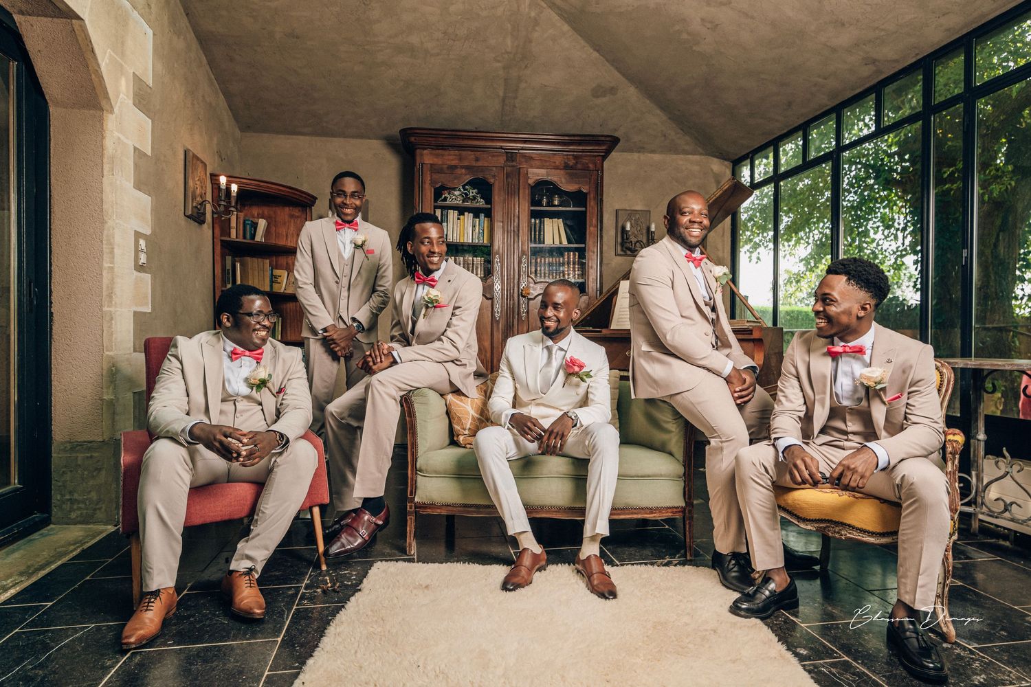 Wedding party in matching beige suits posed casually on indoor porch seating.