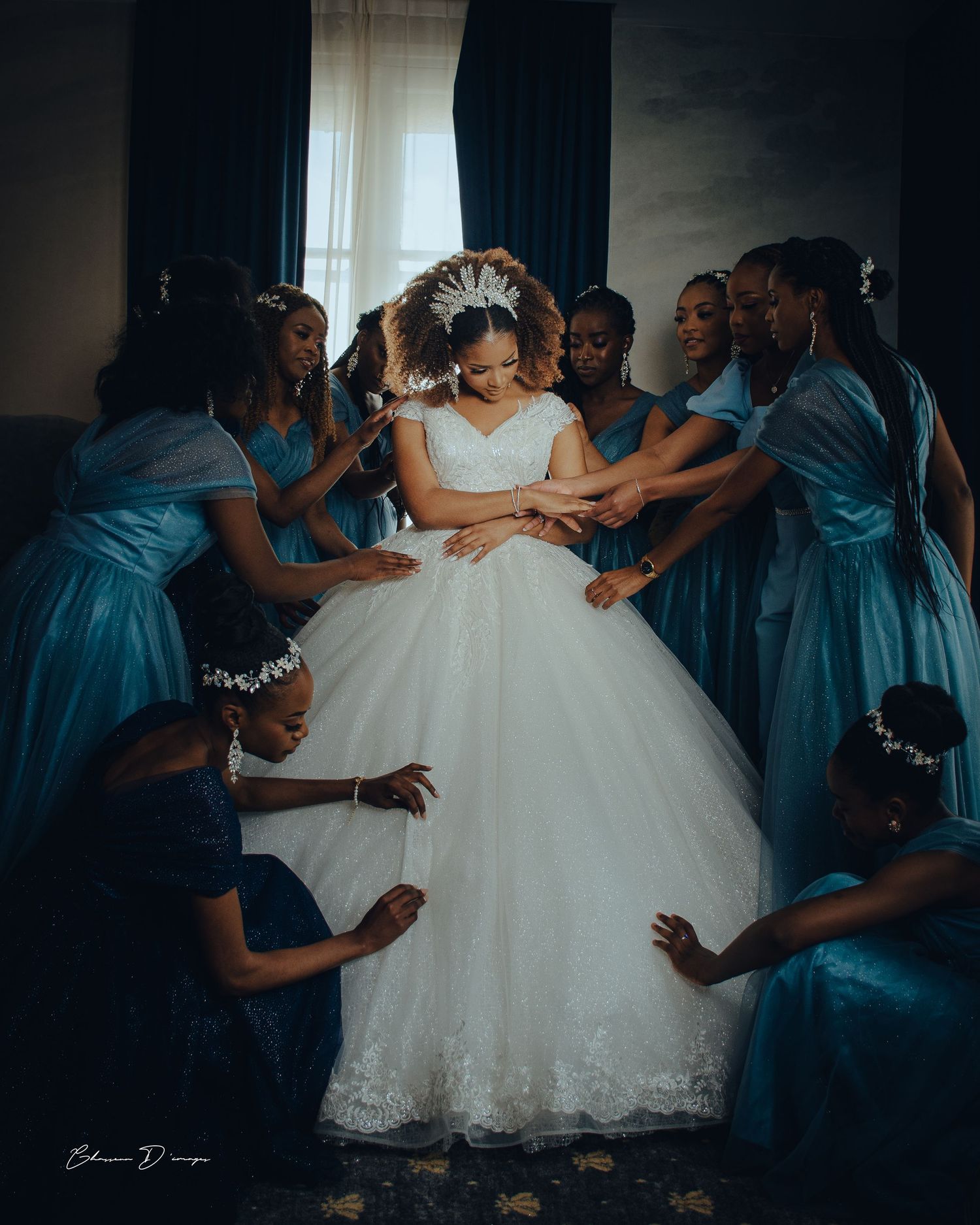 Bridesmaids in matching blue dresses surround and attend to a bride in a white ballgown during an emotional wedding moment.