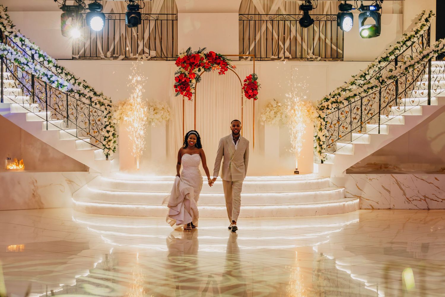 Grand wedding entrance on illuminated staircase decorated with red flowers and sparkling lights.