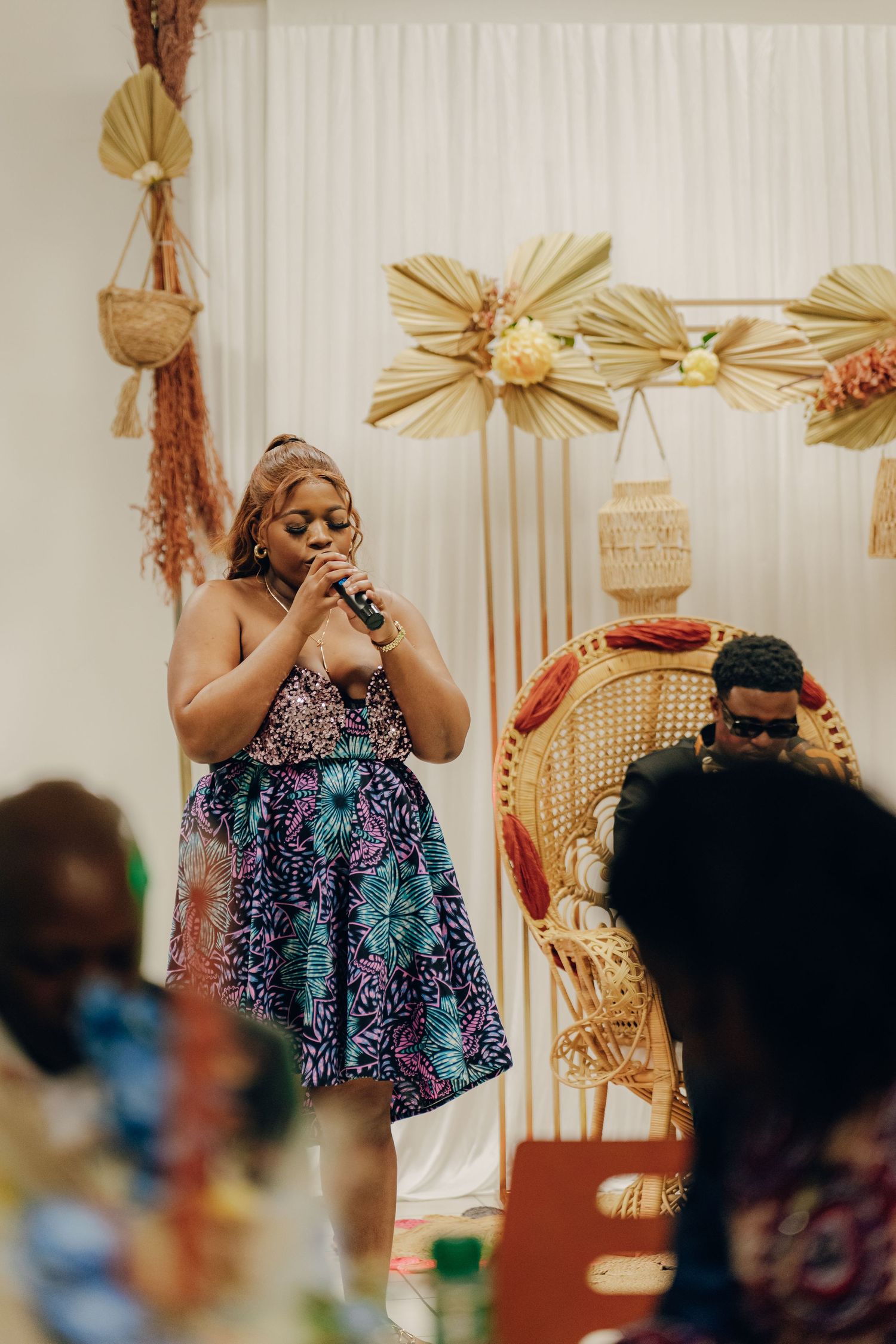 Person in colorful dress speaking into microphone at decorated event venue.