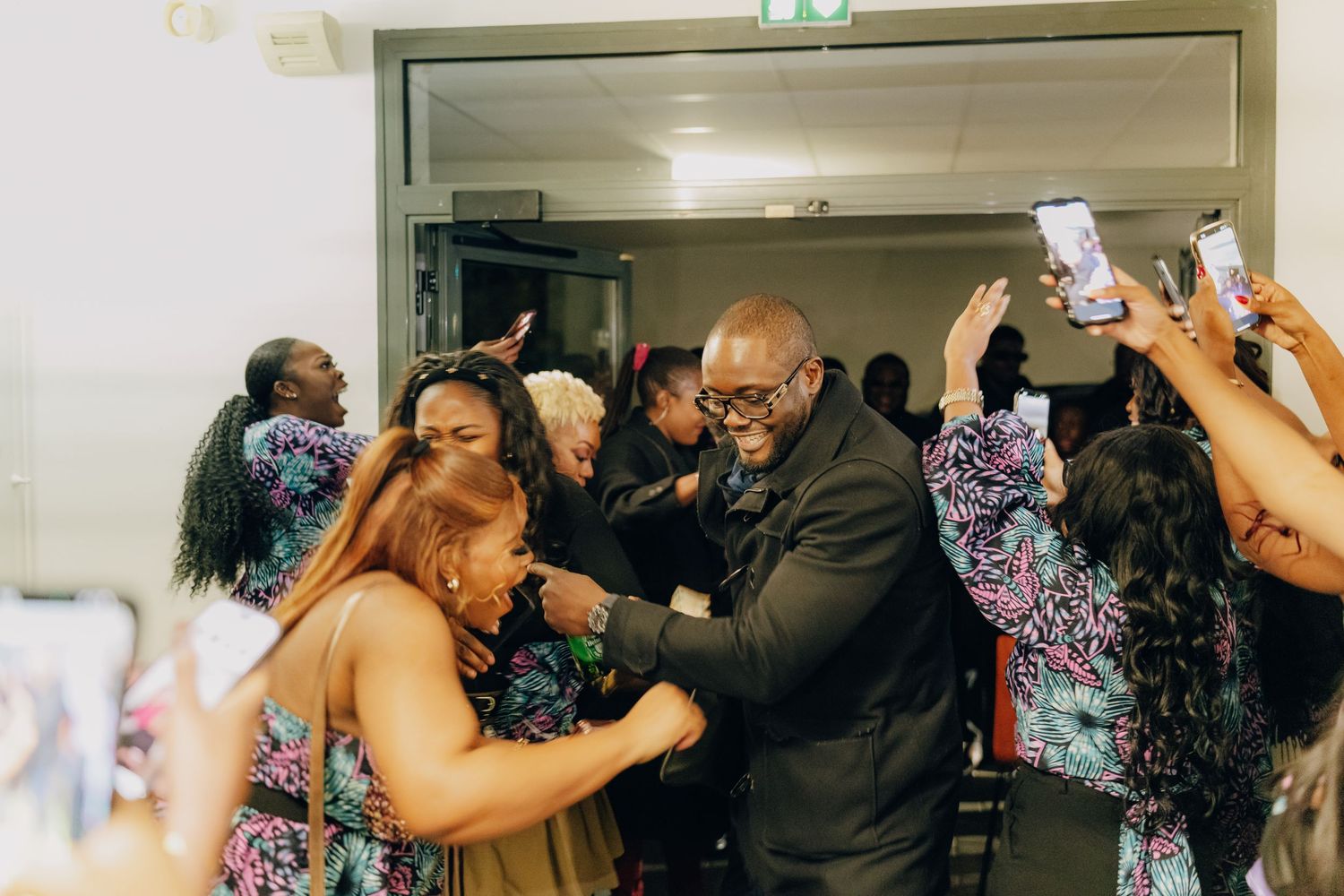 An energetic celebration at an indoor event with people dancing and taking photos with phones raised in the air.