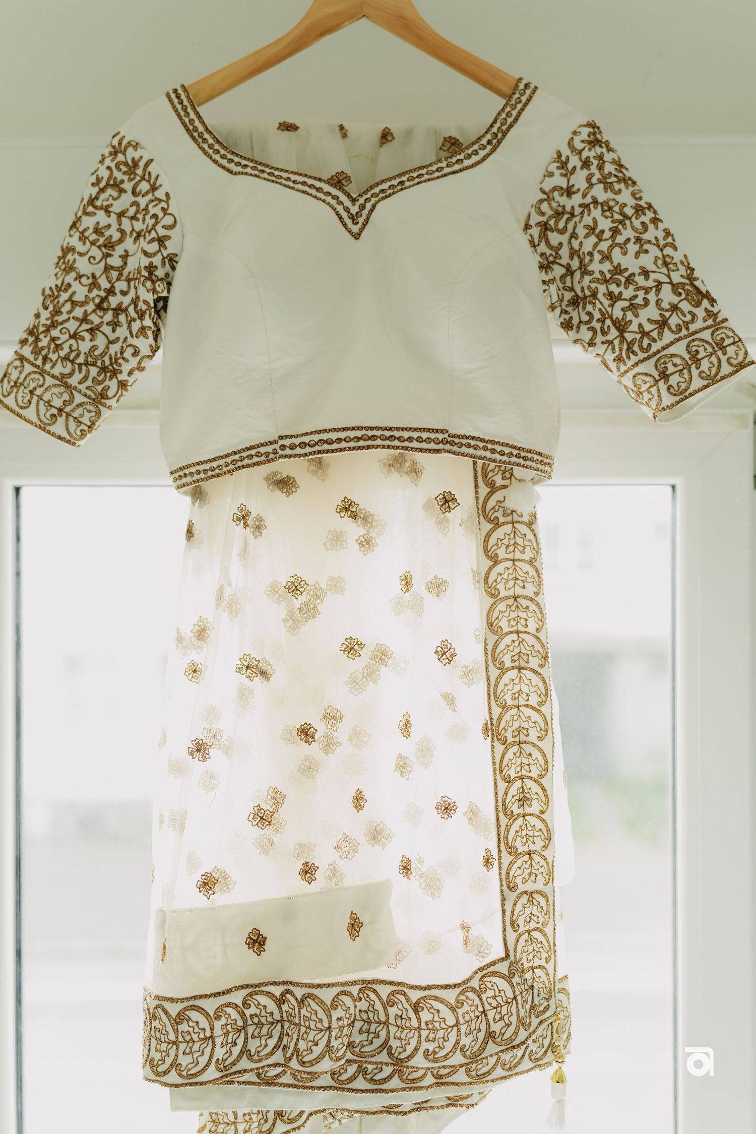 Traditional white Indian outfit with intricate gold embroidery details on sleeves and border displayed on a hanger.