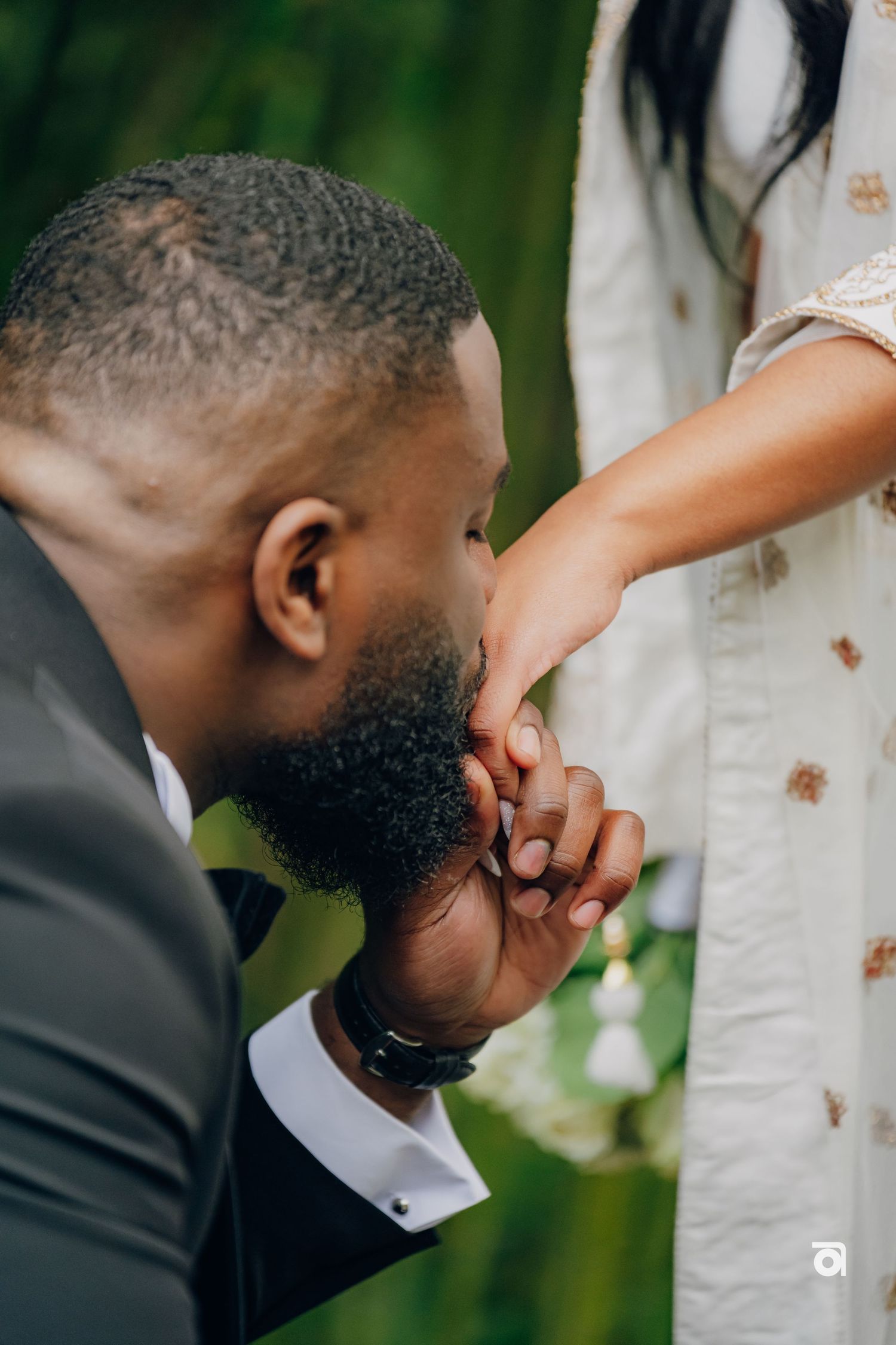A tender moment showing a person in formal attire kissing someone's hand against a soft green background.