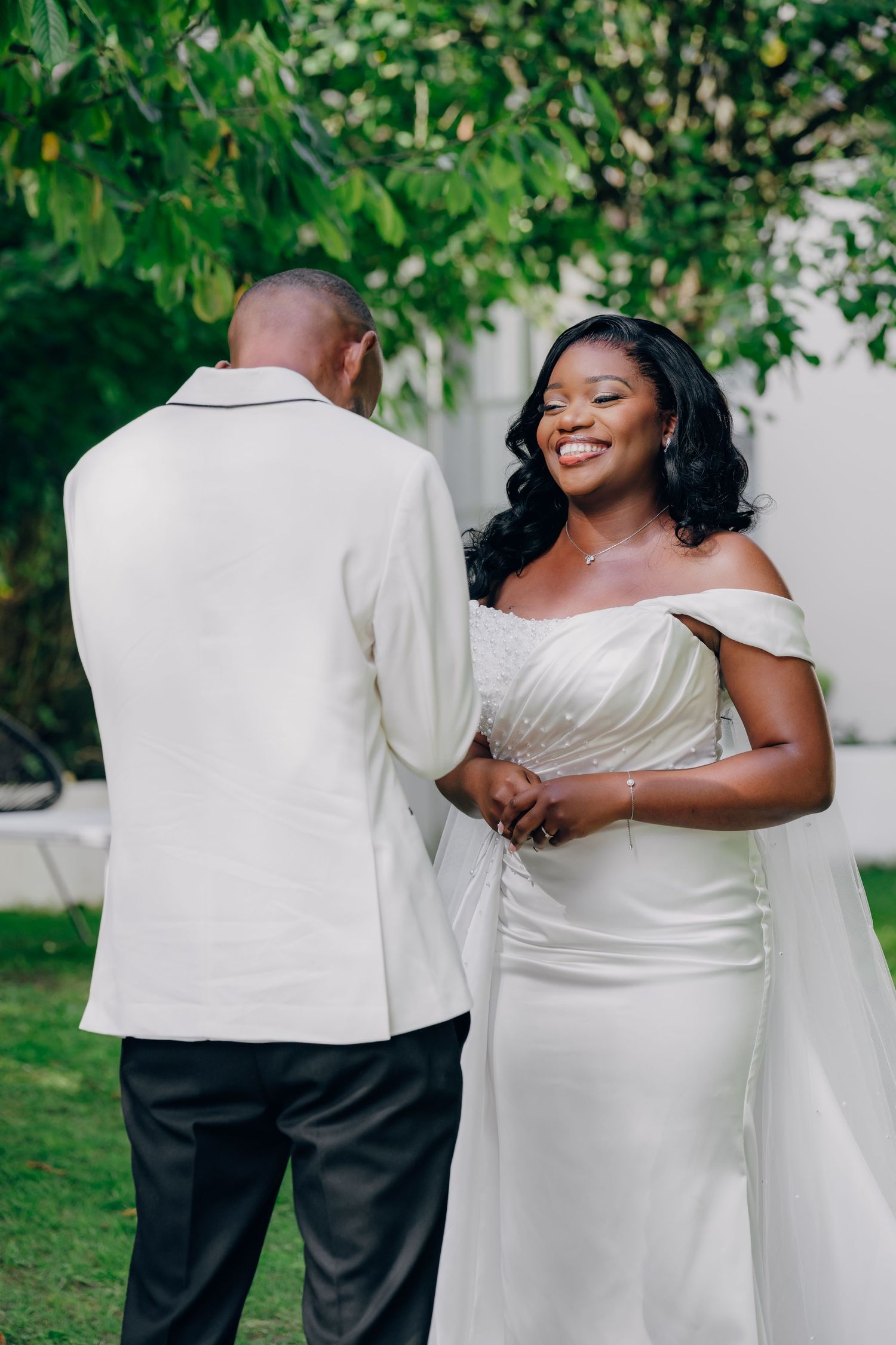 A couple in wedding attire shares intimate moments in a garden setting with green foliage in the background.
