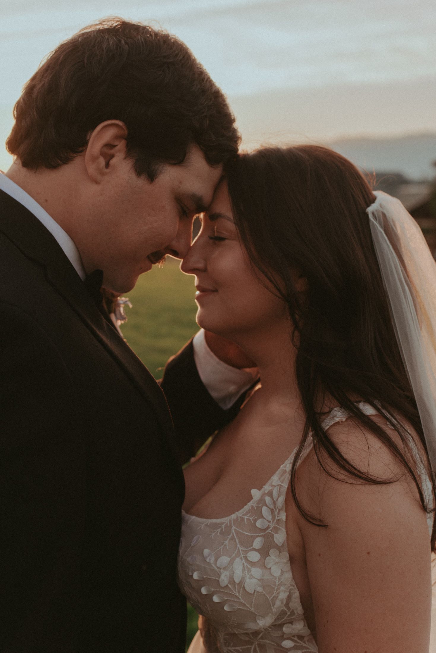 A romantic sunset portrait of a couple in wedding attire sharing an intimate moment outdoors.