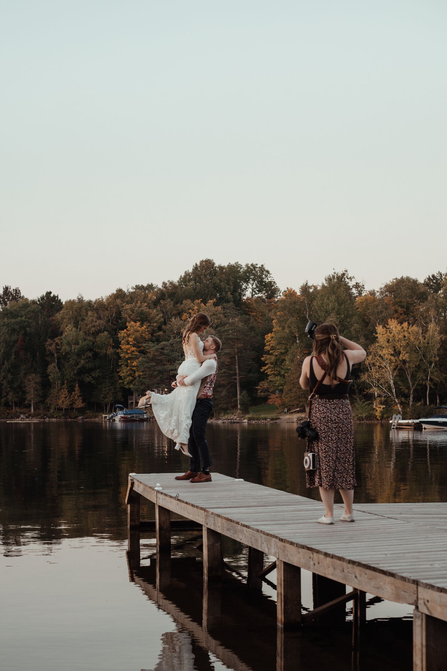 Couple shares a romantic moment on a wooden dock at sunset as photographer captures their wedding photos.
