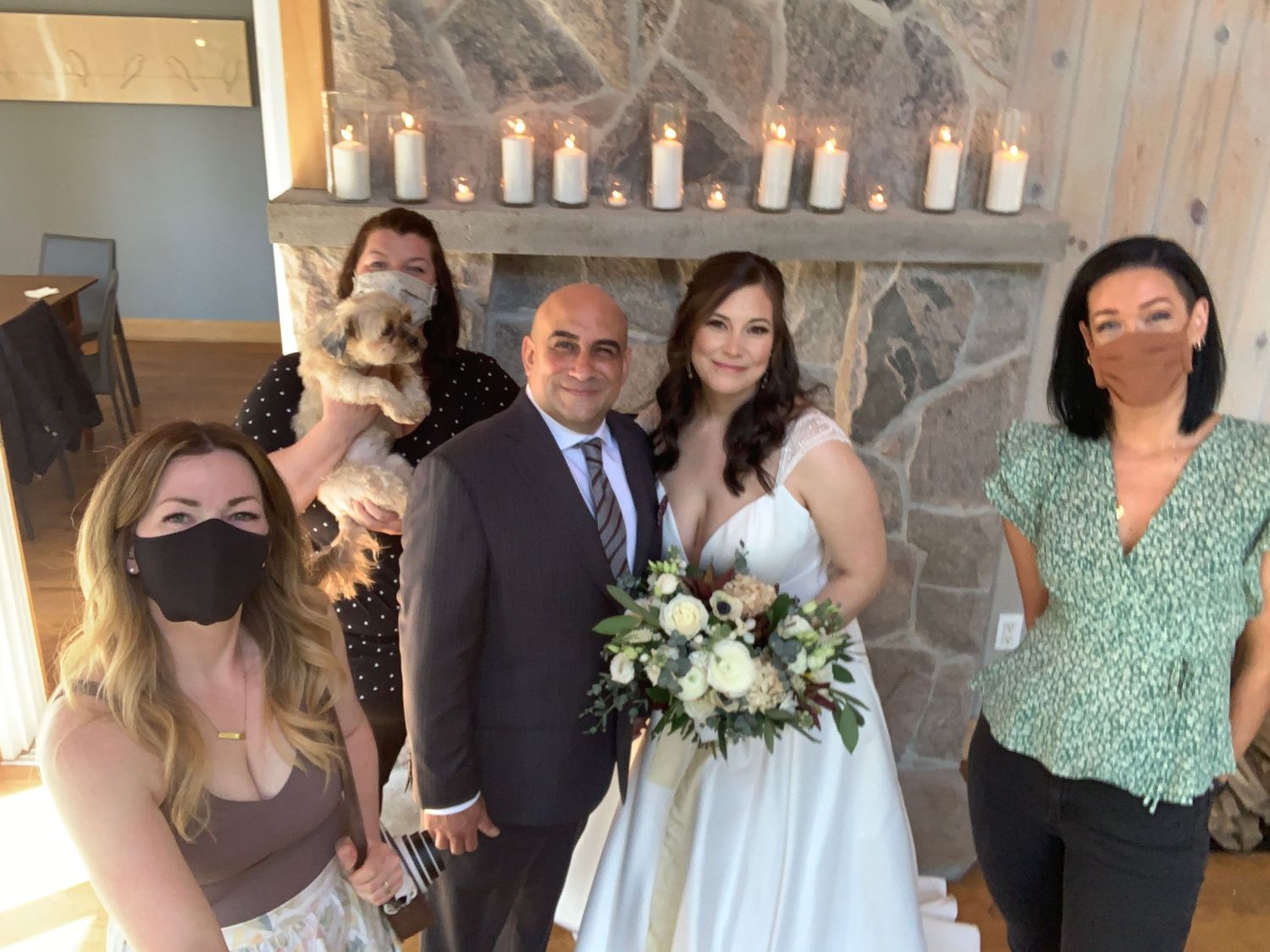 A small group poses for a photo at a wedding ceremony near a stone fireplace with white candles.