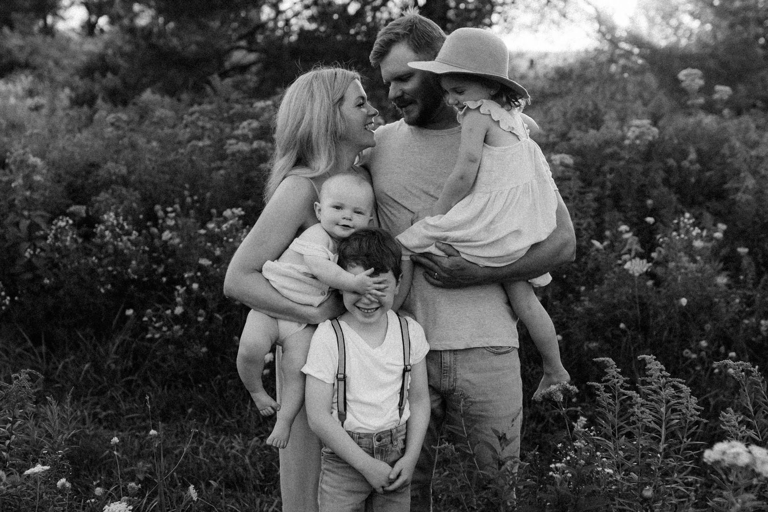 A family shares an intimate moment together outdoors against a natural backdrop of green foliage in black and white.