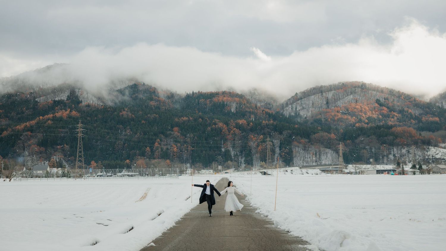 Two figures walking on a snowy path with misty mountains in the background.