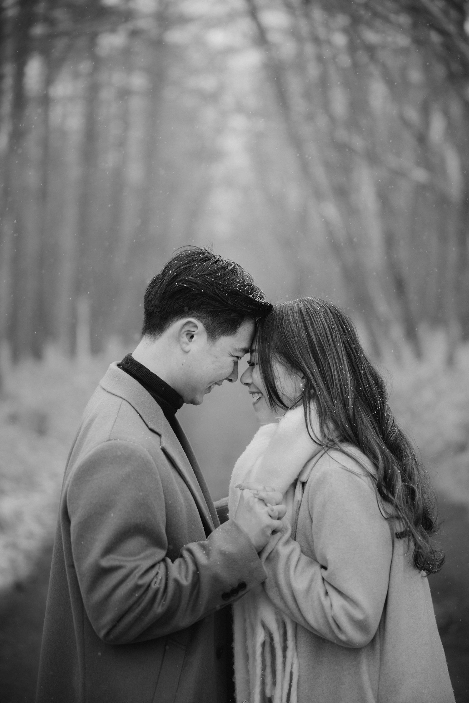 Intimate black and white portrait of a couple in winter coats sharing a tender moment.