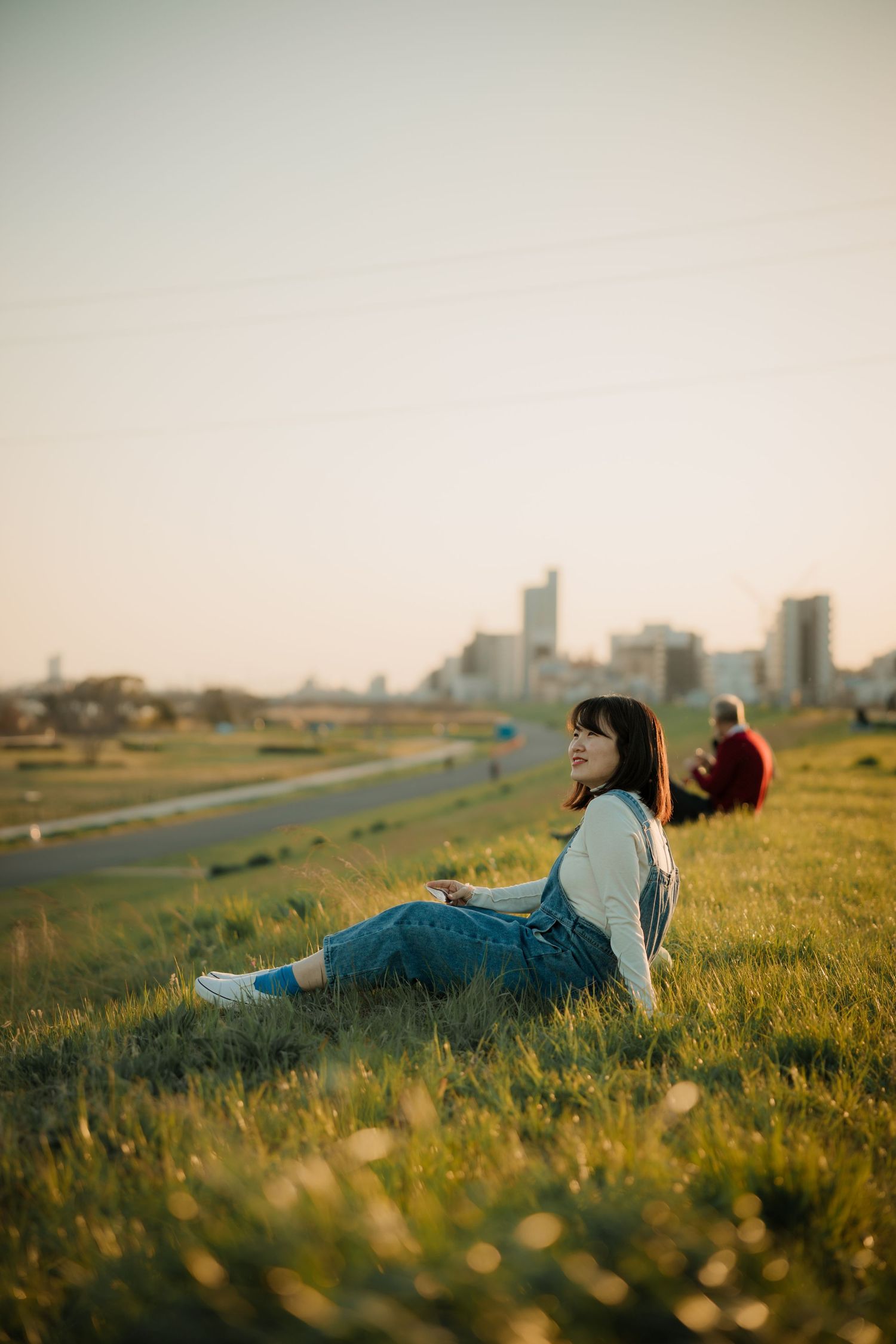 Person relaxing on grassy hill overlooking city skyline at sunset.